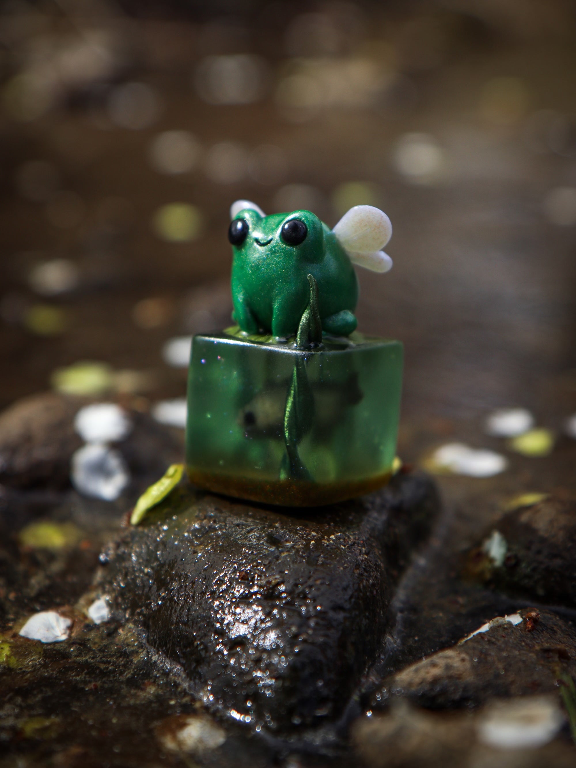 A small green frog figurine with wings perched on a cube, part of the Little Shit Big Deal - CUBES collection by Fairies And Fancies at Strangecat Toys.