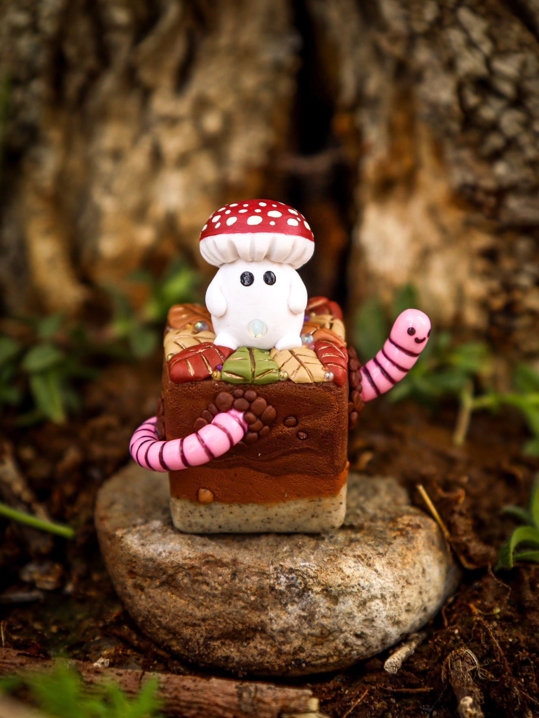 A blind box toy named Little Shit Big Deal - CUBES by Fairies And Fancies, featuring a small toy with a mushroom on a square object, a stone, a mushroom, and a pink worm.