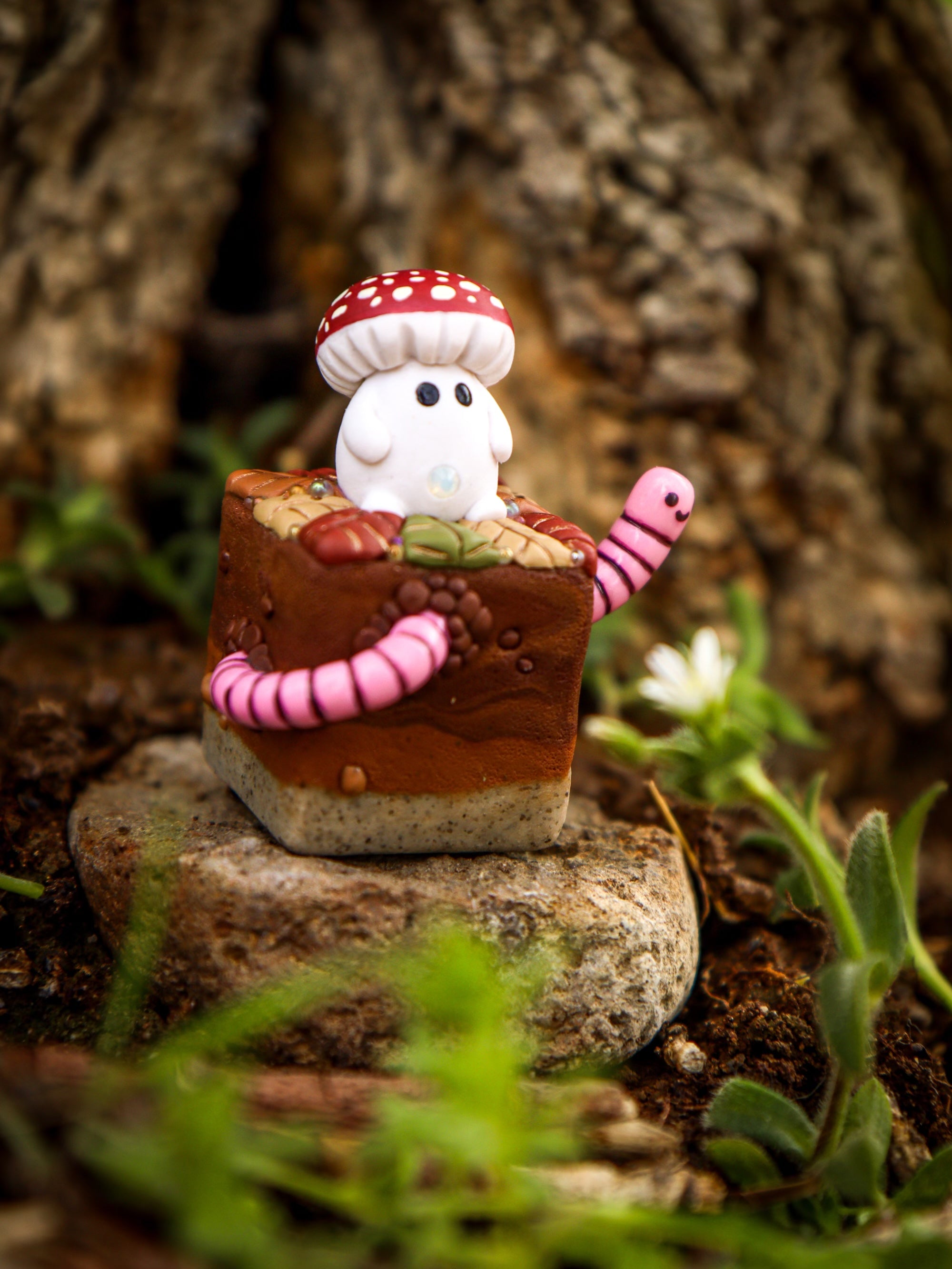 A whimsical clay mushroom and worm figurine on a rock, sculpted by Dr. Polpz. Little Shit Big Deal - CUBES by Fairies And Fancies. A blind box and art toy store.