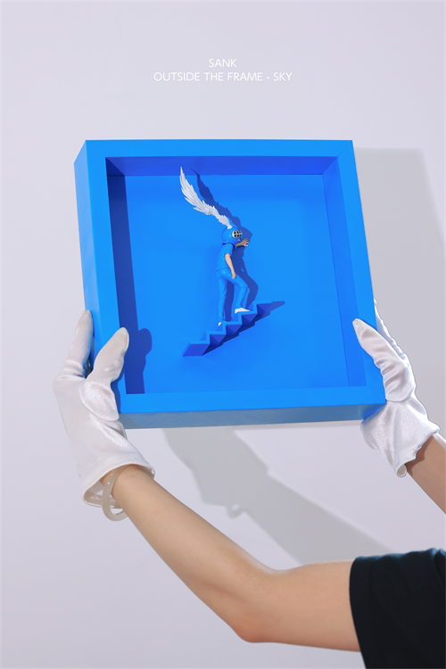 White-gloved hands hold the Sank - Outside the Frame art piece, featuring a blue figurine on a staircase within a shadow box, resembling conceptual art.