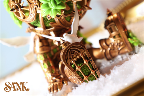 Good Night Series - Sky Wing diorama featuring a gold cage with green succulents, white bird figurines, on faux snow. Preorder for limited edition art piece.