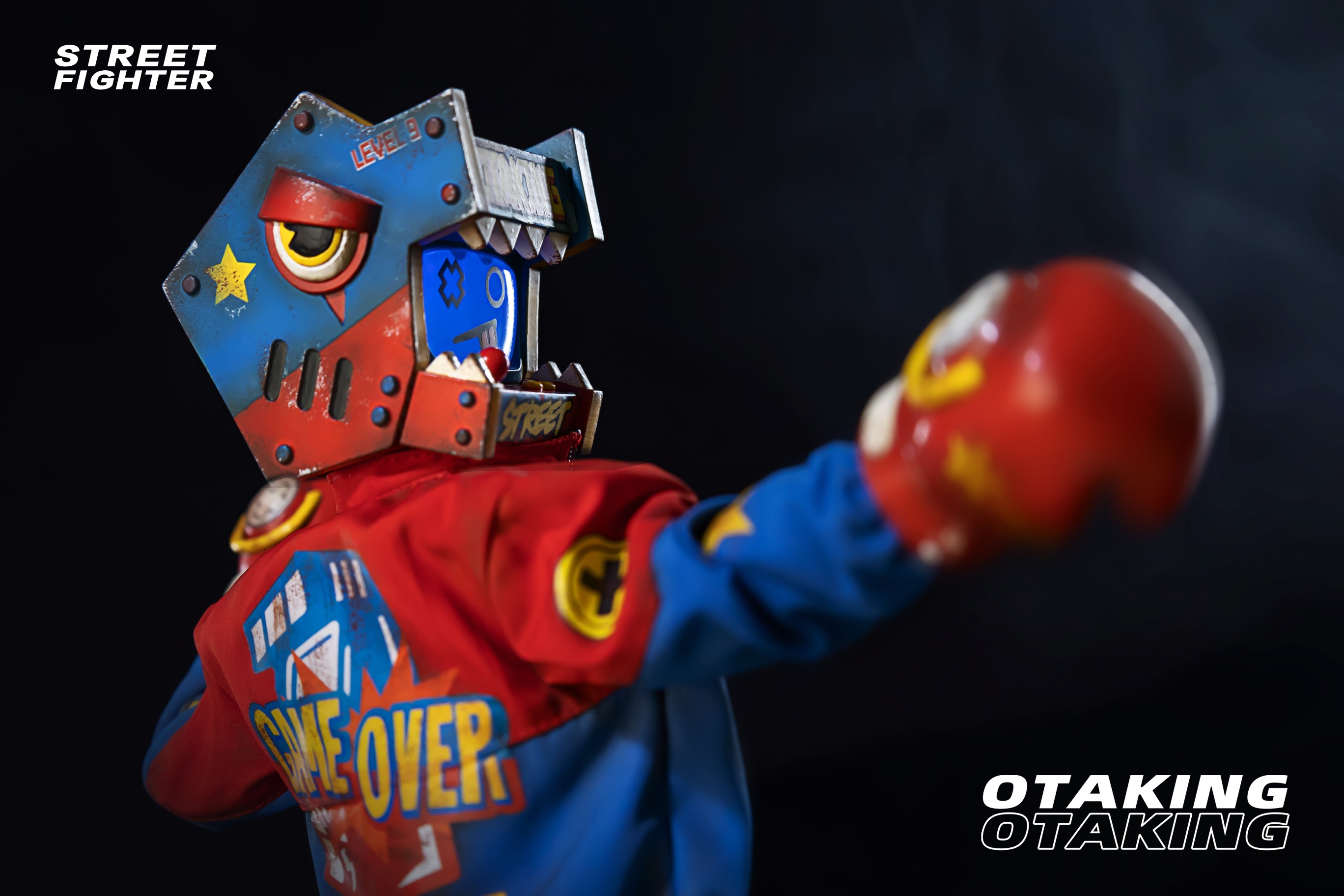 A person wearing a garment, a toy robot, a red boxing glove, and a yellow star on a blue surface, part of the OTAKING - Street Fighter collection.