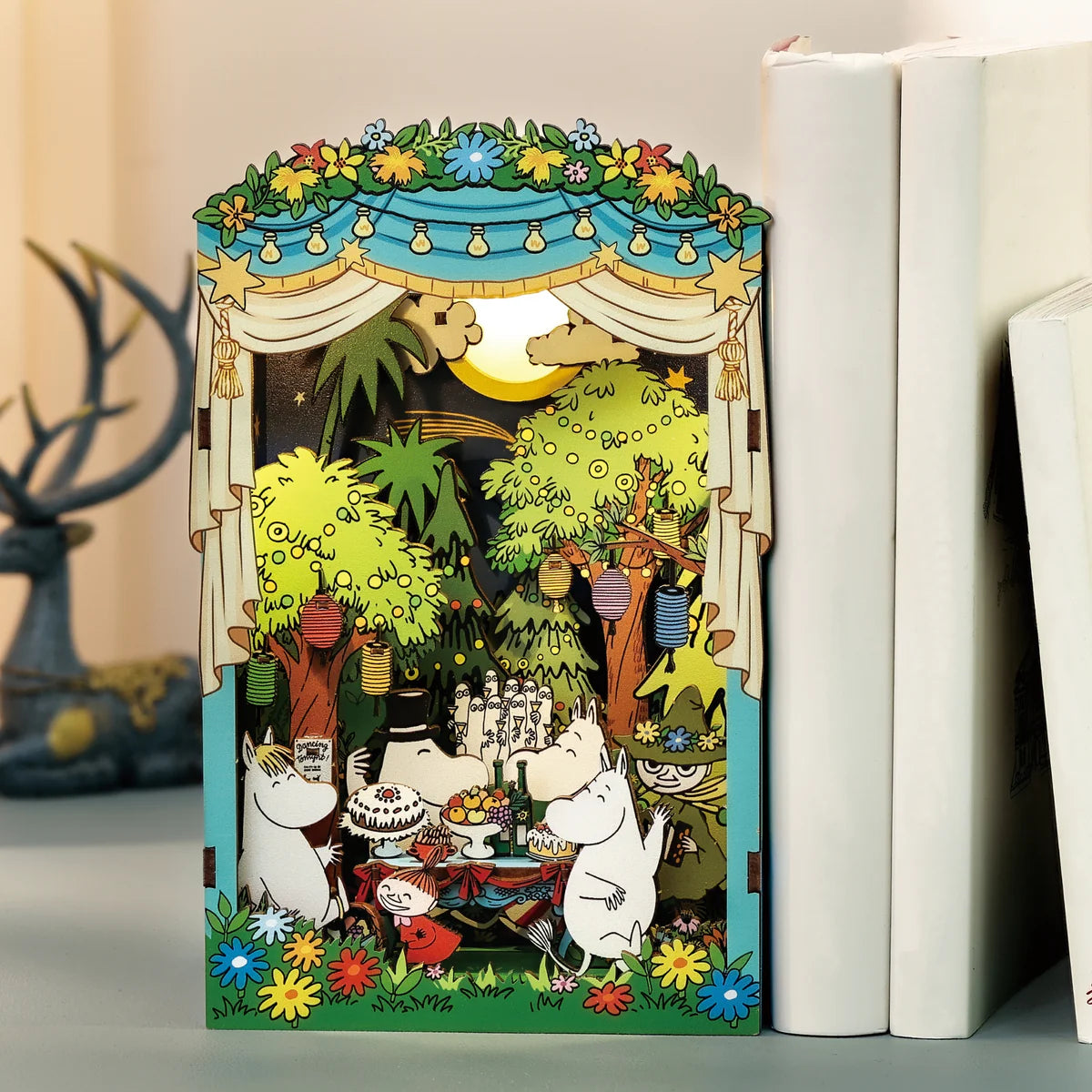 Moomin Moominous Dance Party diorama with Moomin family enjoying an outdoor celebration under lanterns, featuring intricate details and LED light, perfect for bookshelf display.