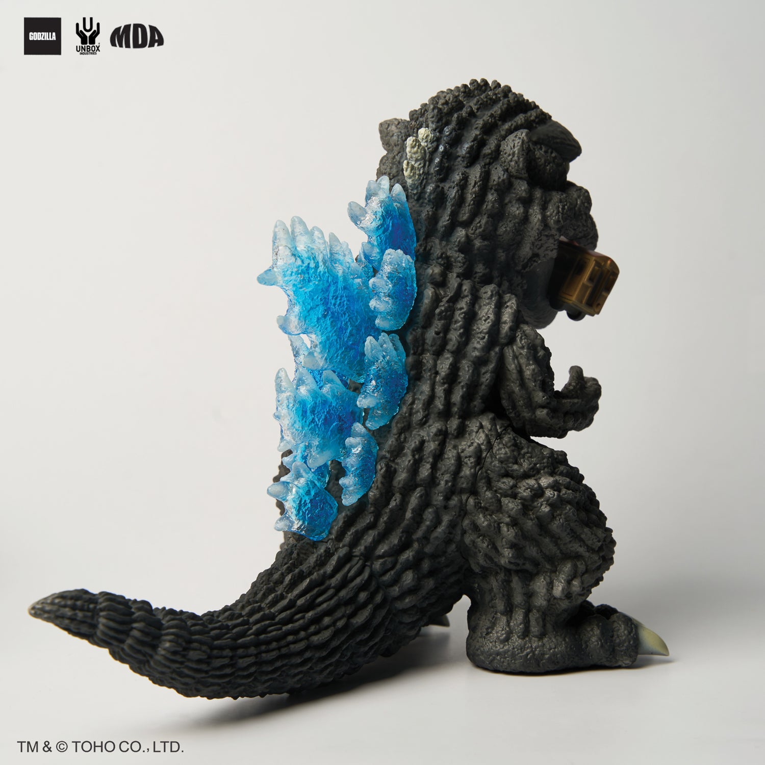 GODZILLA 1954 MDA PROJECT - Preorder: Charcoal-black vinyl figure with textured body, blue atomic dorsal plates, holding a train carriage.
