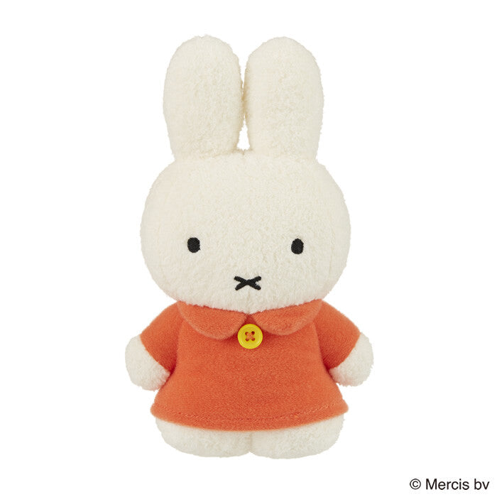Tokotoko Club Miffy plush toy, a small, deformed standing bunny, in an orange dress with a yellow button, evoking a walking stance.
