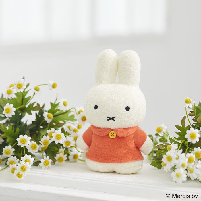 Tokotoko Club Miffy plush toy standing on a white surface, surrounded by daisy-like flowers, showcasing its unique two-head height design and charming expression.