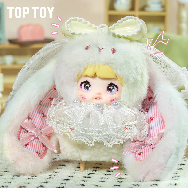Nommi Baby Sweetheart Bunny Plush Blind Box doll in a fluffy bunny hood with lace ruffle and pearl accents, styled in a toy display.