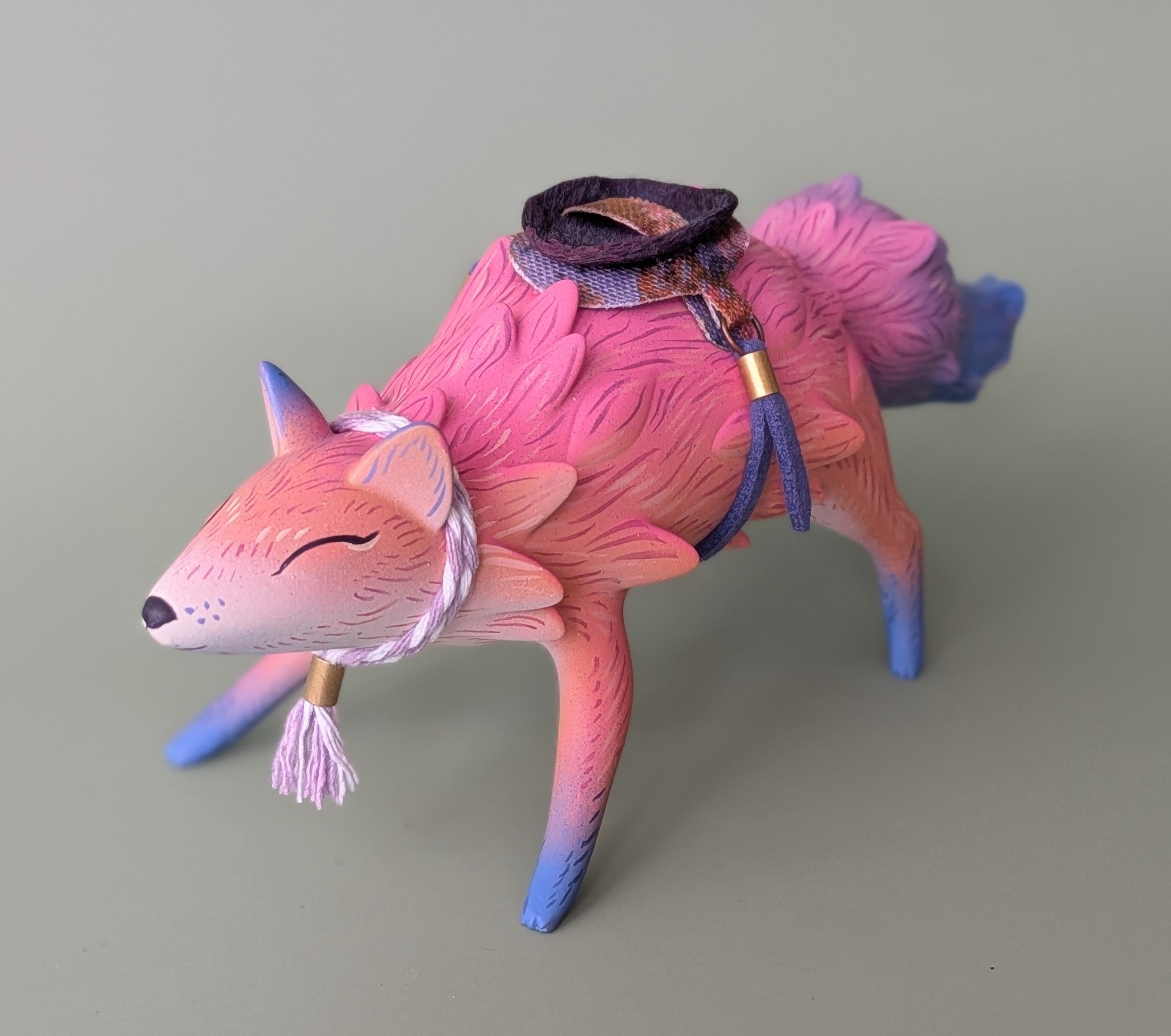 A handcrafted resin figurine of a sleeping fox-like creature, featuring intricate textures and a tiny saddle, titled ORACLE Group Show - A Familiar Friend.