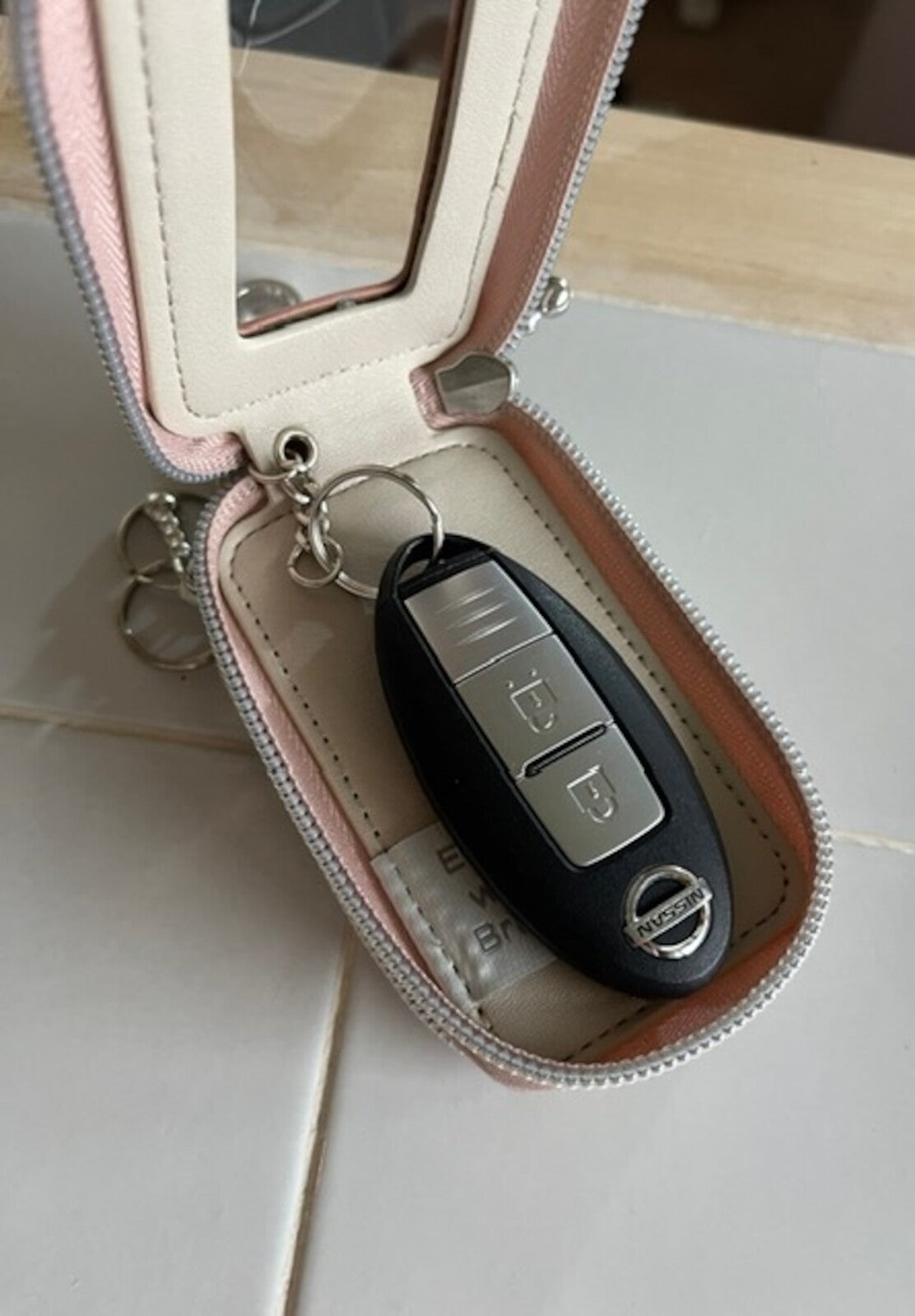 Miffy Key Case open on tiles, displaying a Nissan key fob inside. Features a mirror and bag attachment for easy access to keys.
