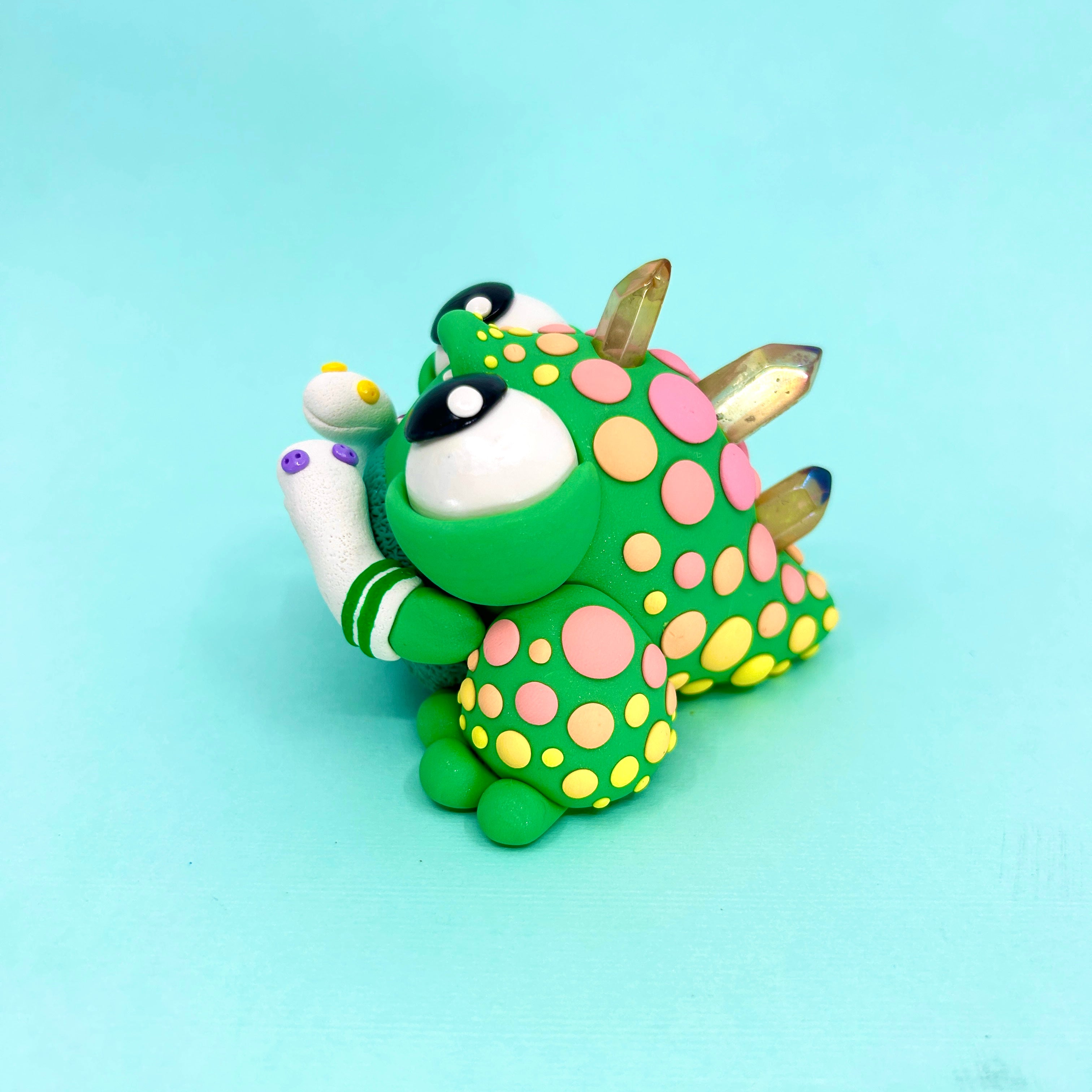 A small dinosaur toy with colorful crystals and dots, part of Simon Says Macy & Friends - Clementine and Her Only Friends collection.
