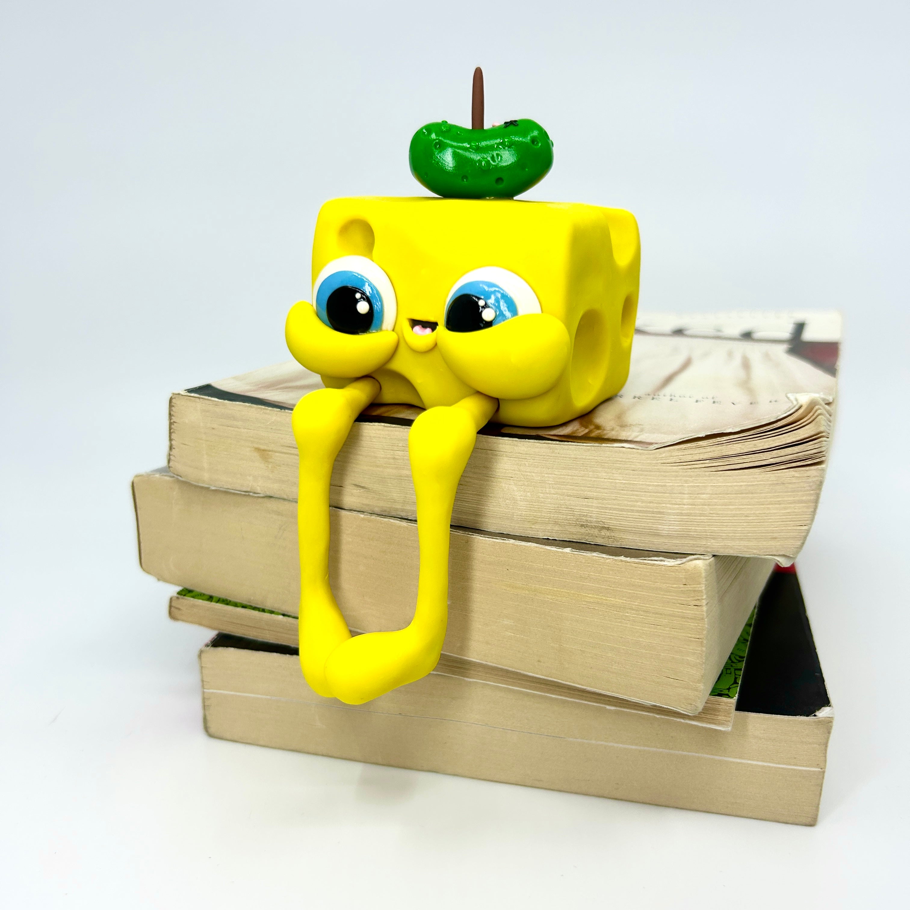 Toy with legs and eyes on books, next to a green apple stick.