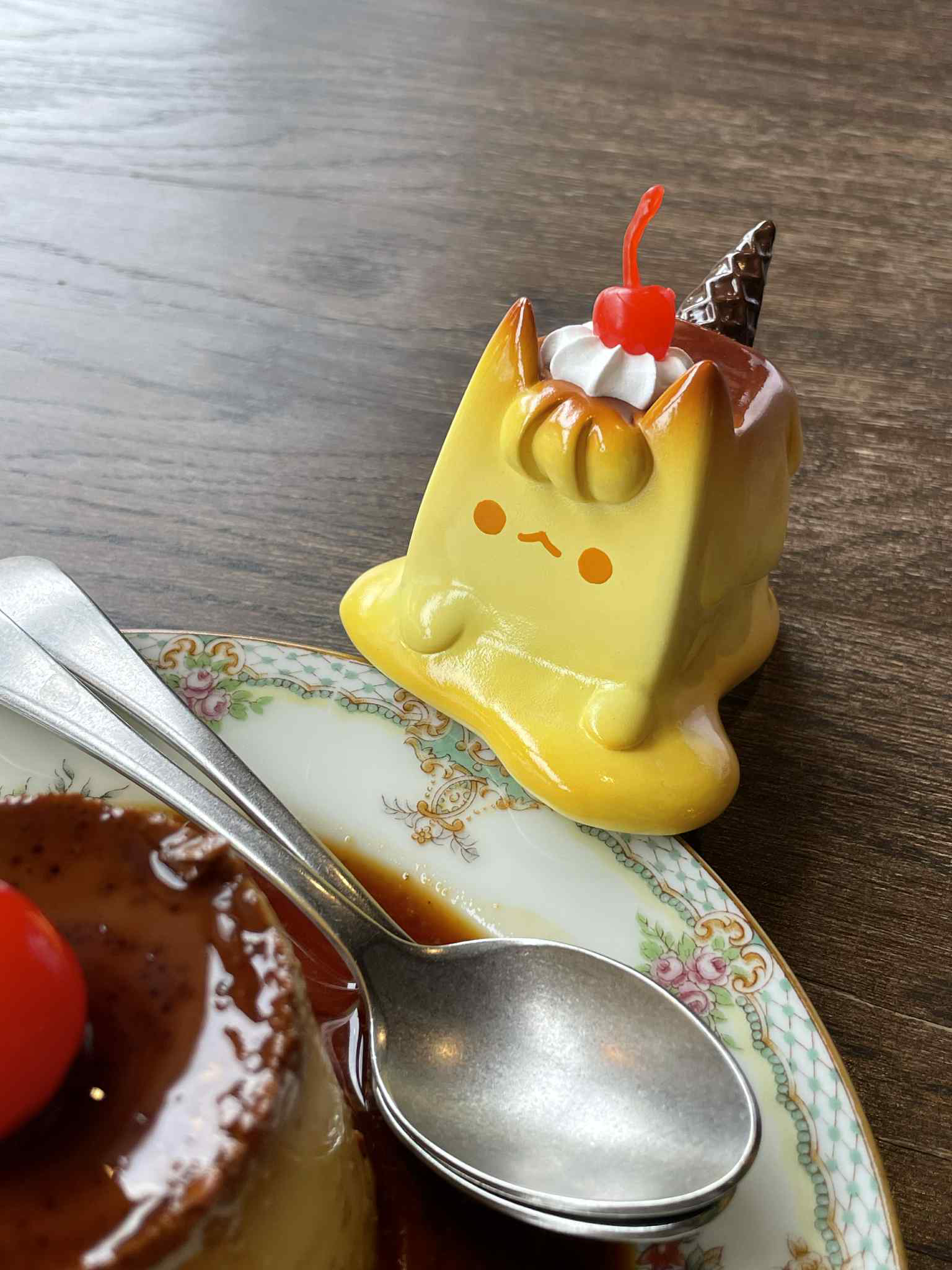 Pudding Cat by Rato Kim: A glossy yellow, cat-shaped sofubi figurine with whipped cream, cherry, and waffle-cone topping, resembling a melting pudding.