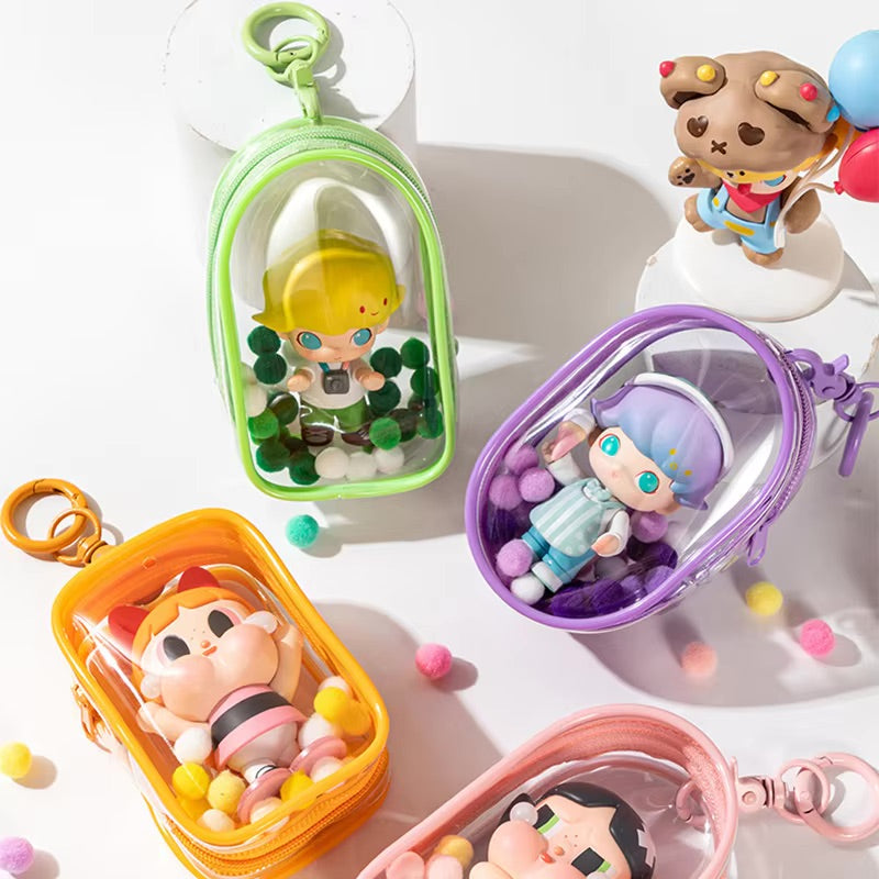 Toy Pochette Clip Keychain displayed among small plastic toys, featuring a clear case and bag. PVC material, sold as one doll bag, without dolls.