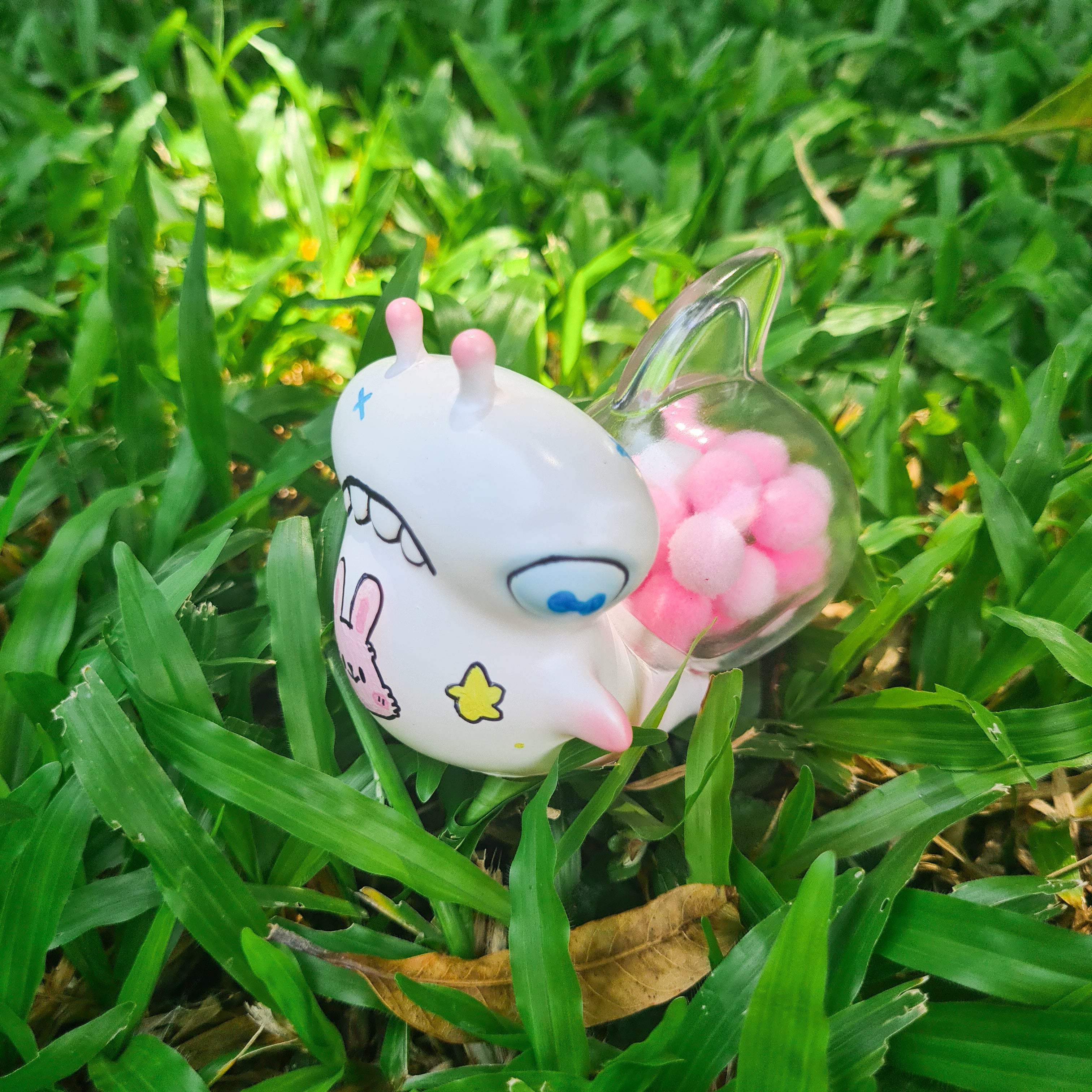 Plastic snail toy with candy shell, pink balls in container, and yellow star on white surface.