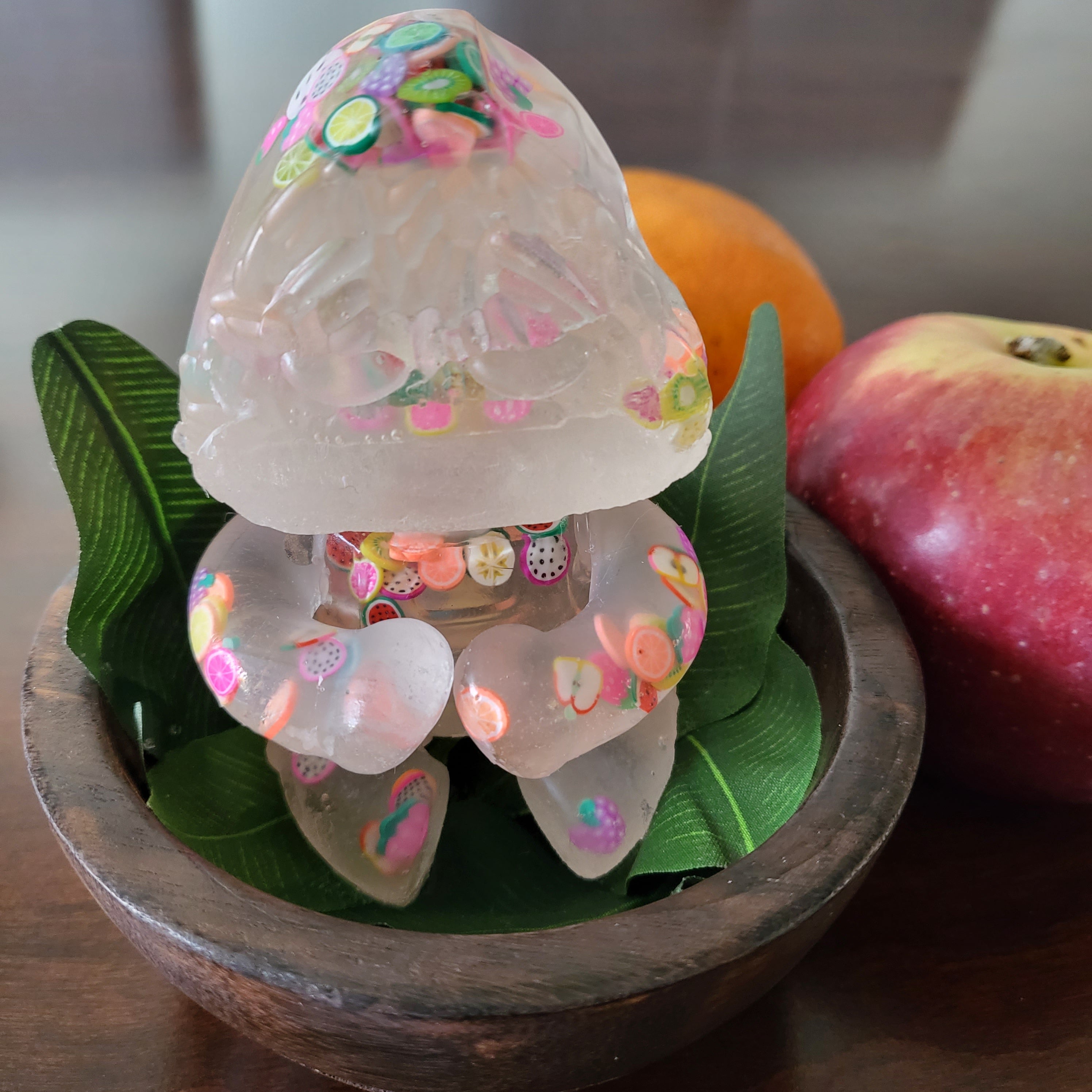 A jelly-like creature in a bowl with leaves, an apple, and other fruity objects.