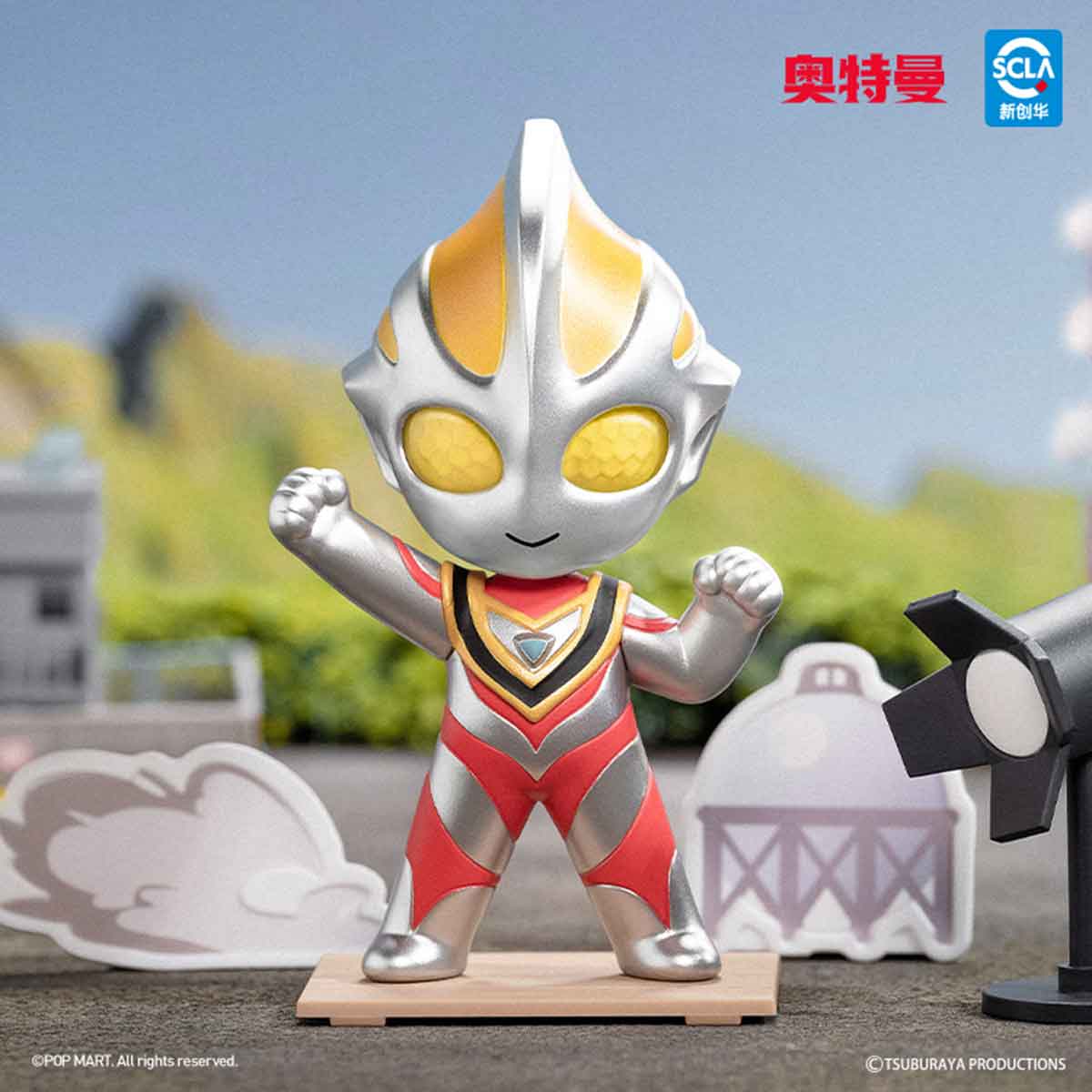 Ultraman Shooting Studio Series figure in chibi style, posed with fists raised on a display base, surrounded by mini diorama scenery and branding elements.