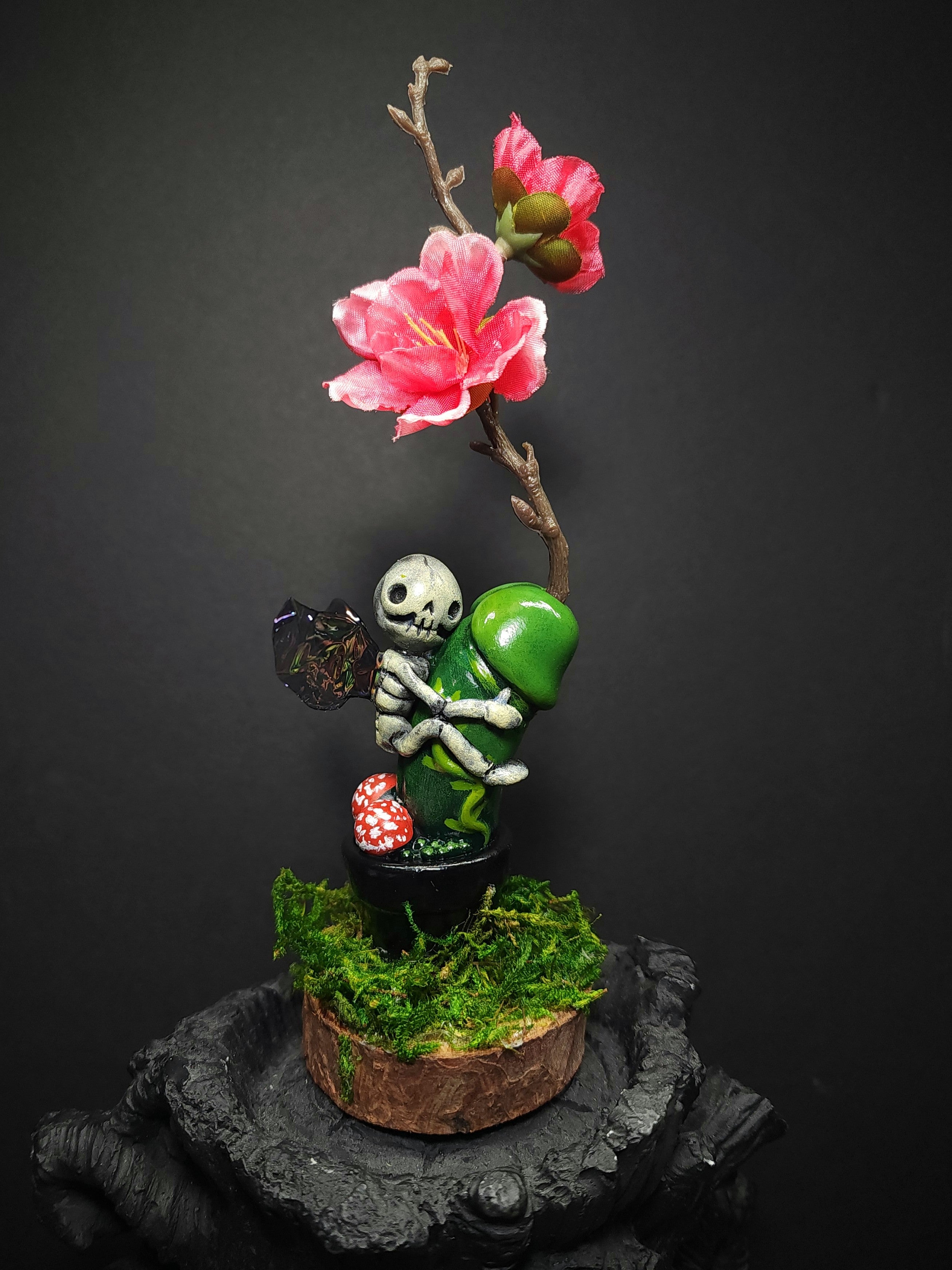 Polymer Clay statue of skeleton with mushroom and flower, green plant on stump, and pink flower on branch by Simon Says Macy & Friends - Prick Riding Fairy.