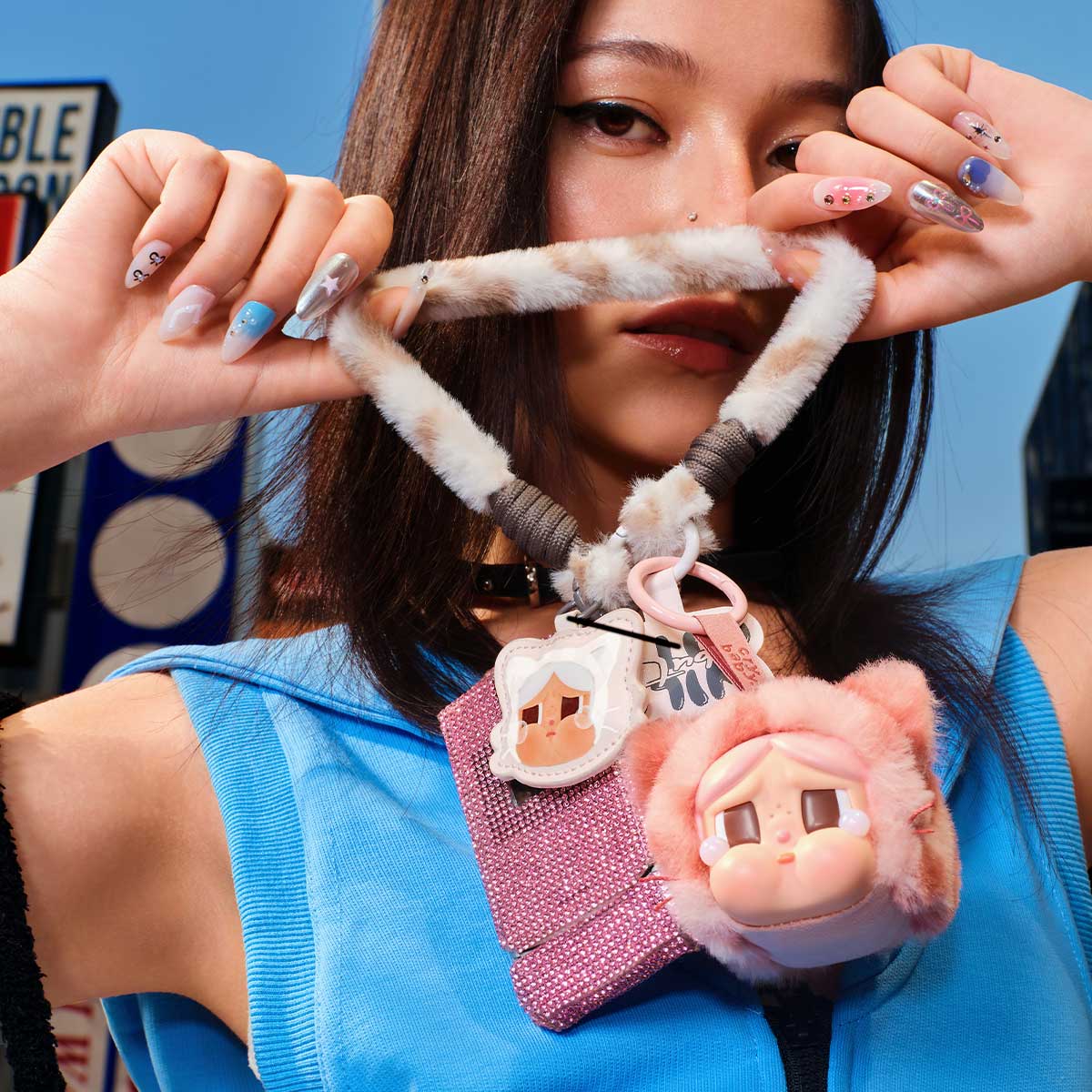 Young woman displays a CRYBABY Wild but Cutie Series Vinyl Plush Pendant, featuring a fuzzy strap with cute accessories, highlighting multicolored nail art.
