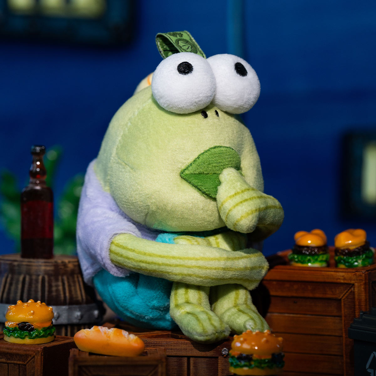 Bikini Bottom Buddies - Whimsical Plush: A soft green creature sits among toy hamburgers, staged on wooden crates, evoking a diorama-like, playful scene.
