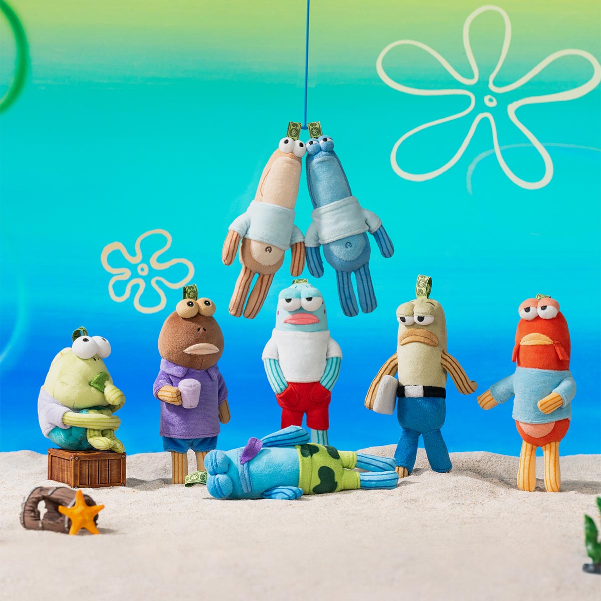 Bikini Bottom Buddies - Whimsical Plush set displayed on sandy surface with underwater backdrop, featuring seven toys and two hanging above, plus a crate and starfish prop.