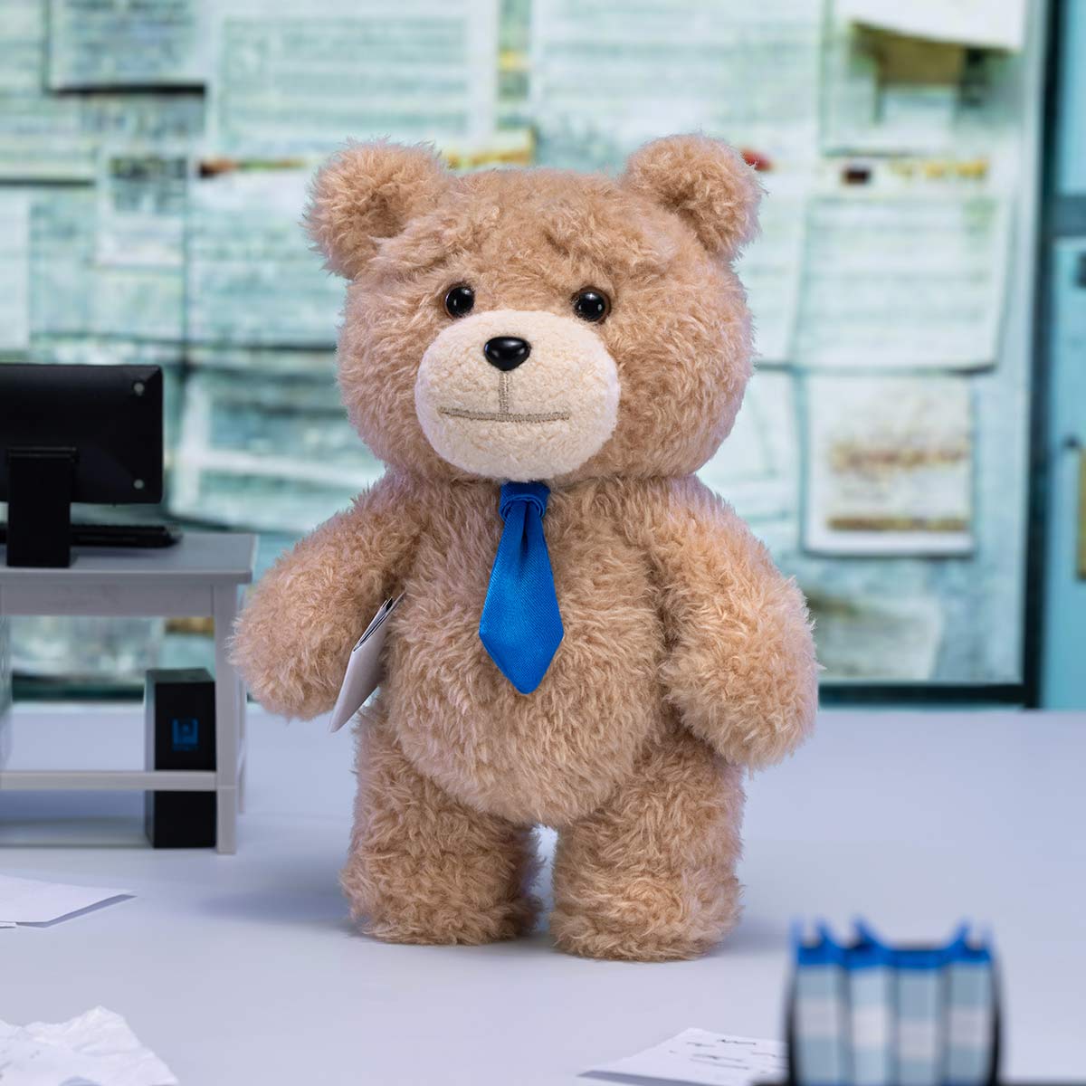 Ted2 Teddy Bear Action Plush Pendant holding a paper, wearing a blue necktie, displayed on an office desk. Part of a collectible series from Strangecat Toys.