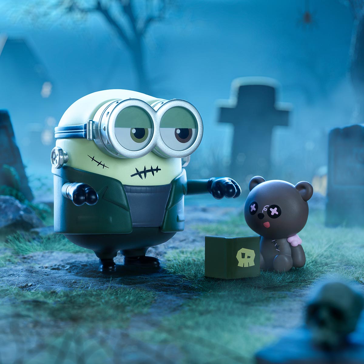 Minions Bedtime Stories figure as Frankenstein in a graveyard scene, featuring stitched scars, goggles, jacket, teddy bear, skull, and box with skull emblem.