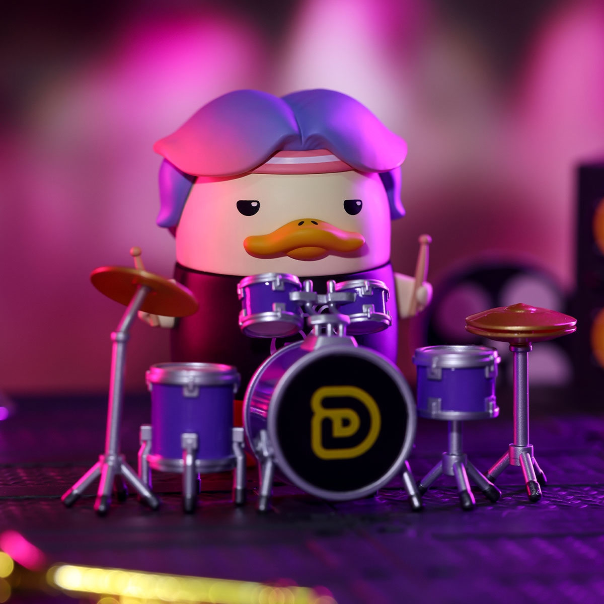 DUCKOO Music Festival Series toy duck drumming behind a miniature kit, featuring purple hair and a pink headband. Preorder for October 2025 shipping.