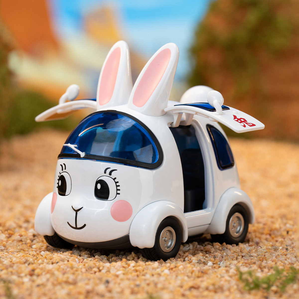 Cartoon rabbit toy car from DRAGON BALL-Alloy Vehicles Series with bunny ears, on sand, featuring a smiling face and translucent blue windows.