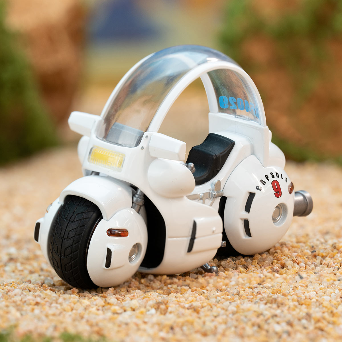 Futuristic toy vehicle model from DRAGON BALL-Alloy Vehicles Series Figures, featuring a glossy white design with CAPSULE 9 marking, displayed on gravel.