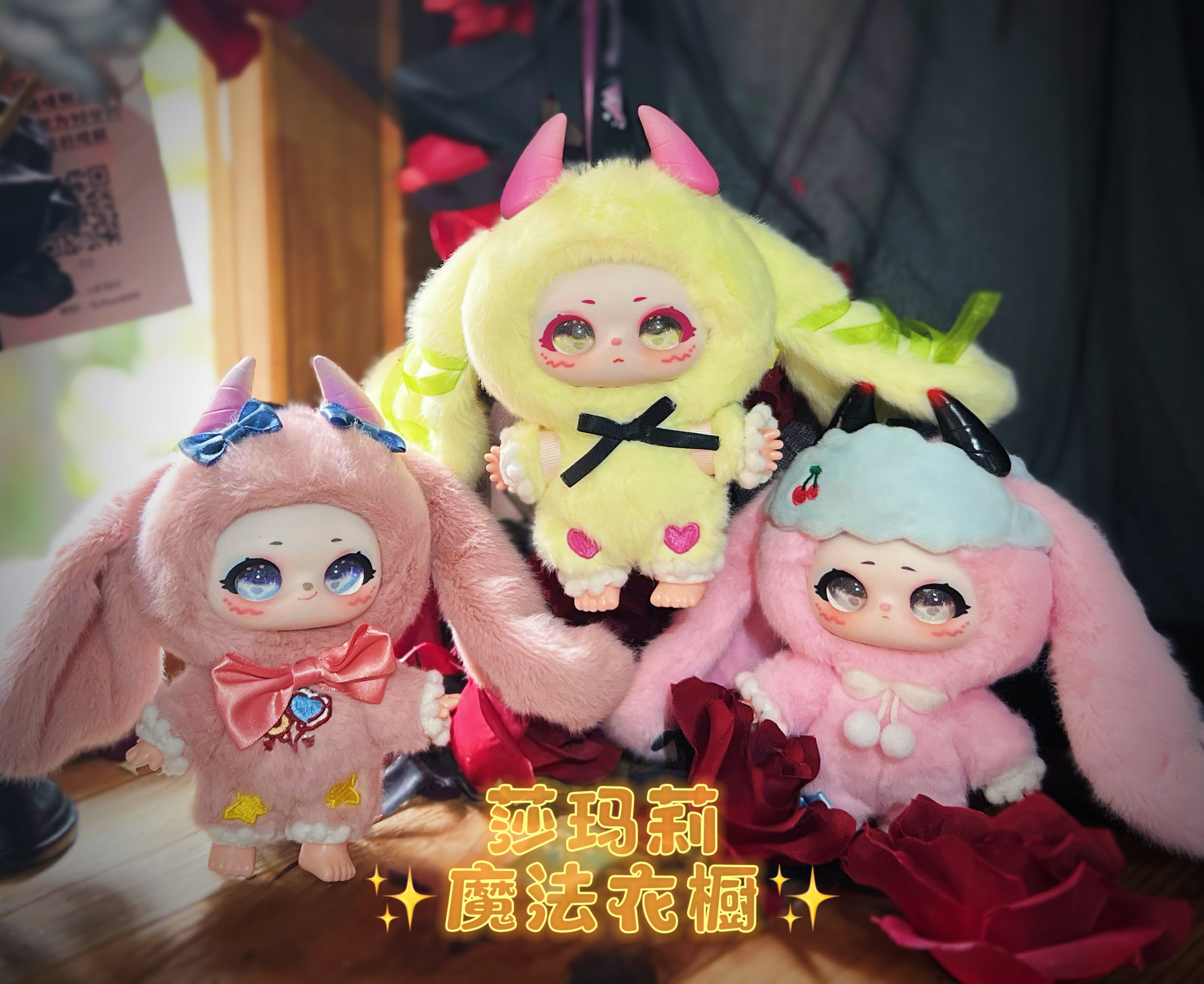 Three Baby Three dolls in bunny onesies with horns, displayed with rose petals, promoting Shamali Magic Wardrobe preorders at Strangecat Toys.