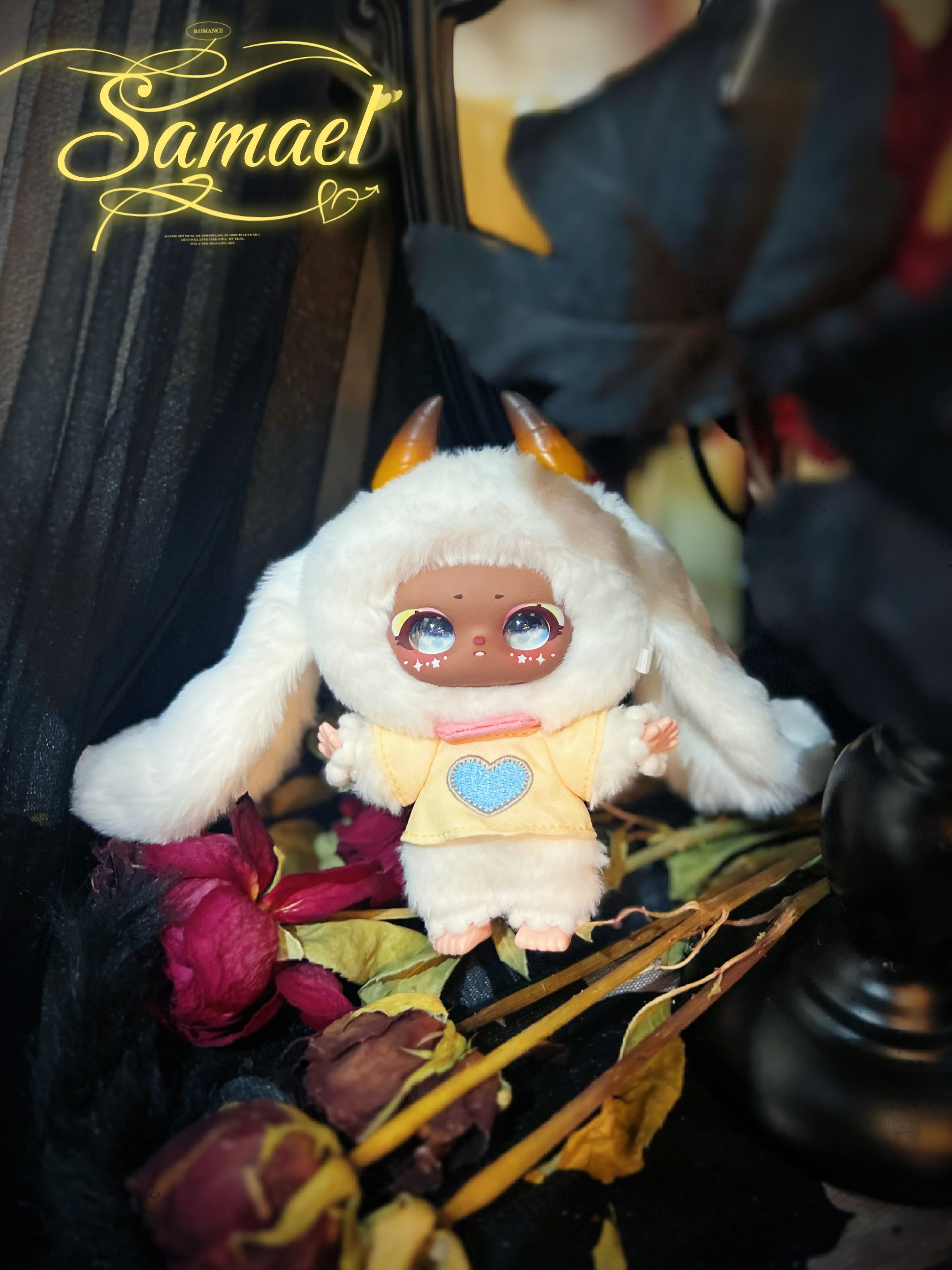 Baby Three - Shamali Magic Wardrobe figurine in a bunny costume with glittering eyes and star motifs, posed among dried roses, titled Samael.