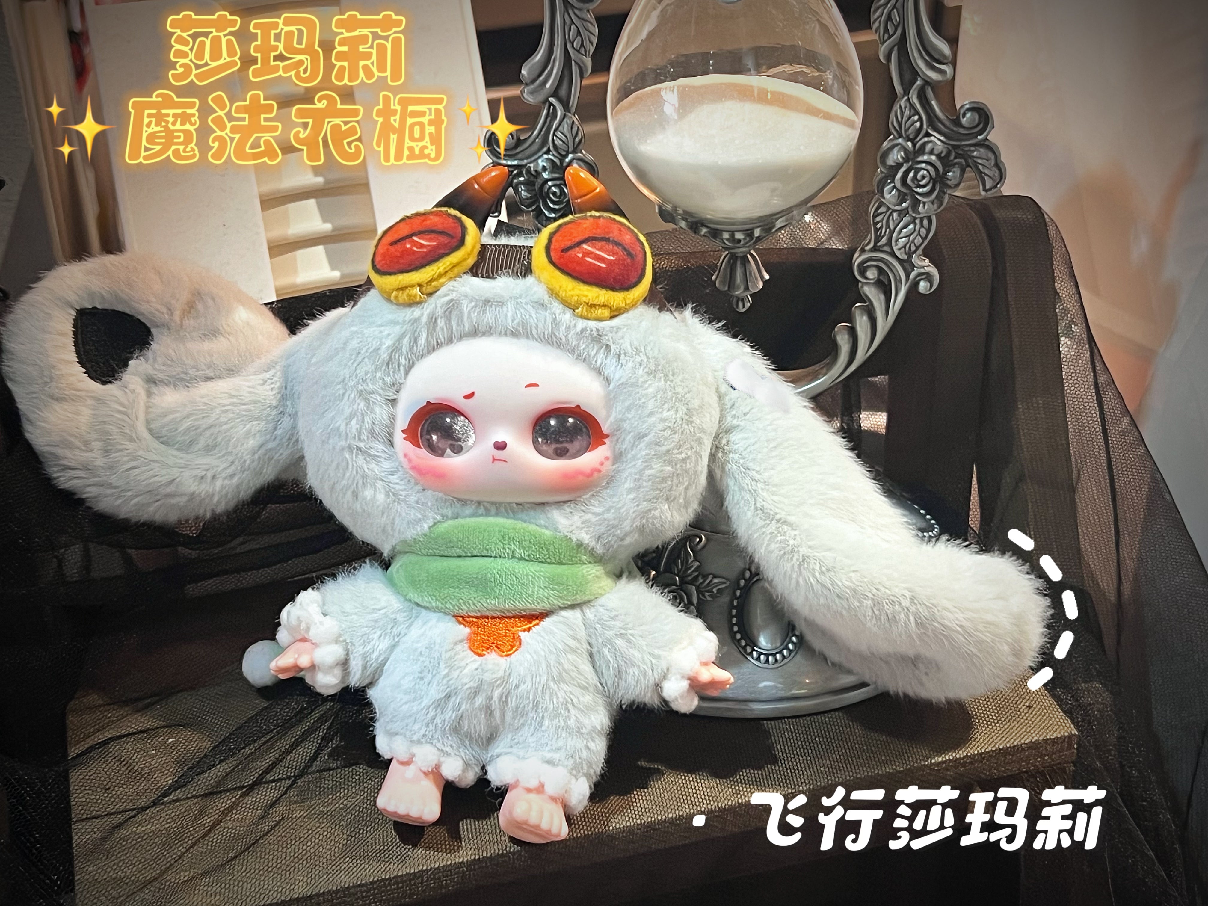 Collectible Baby Three - Shamali Magic Wardrobe doll in a fluffy bunny suit with goggles, set before a silver-framed hourglass. Preorder now from Strangecat Toys.