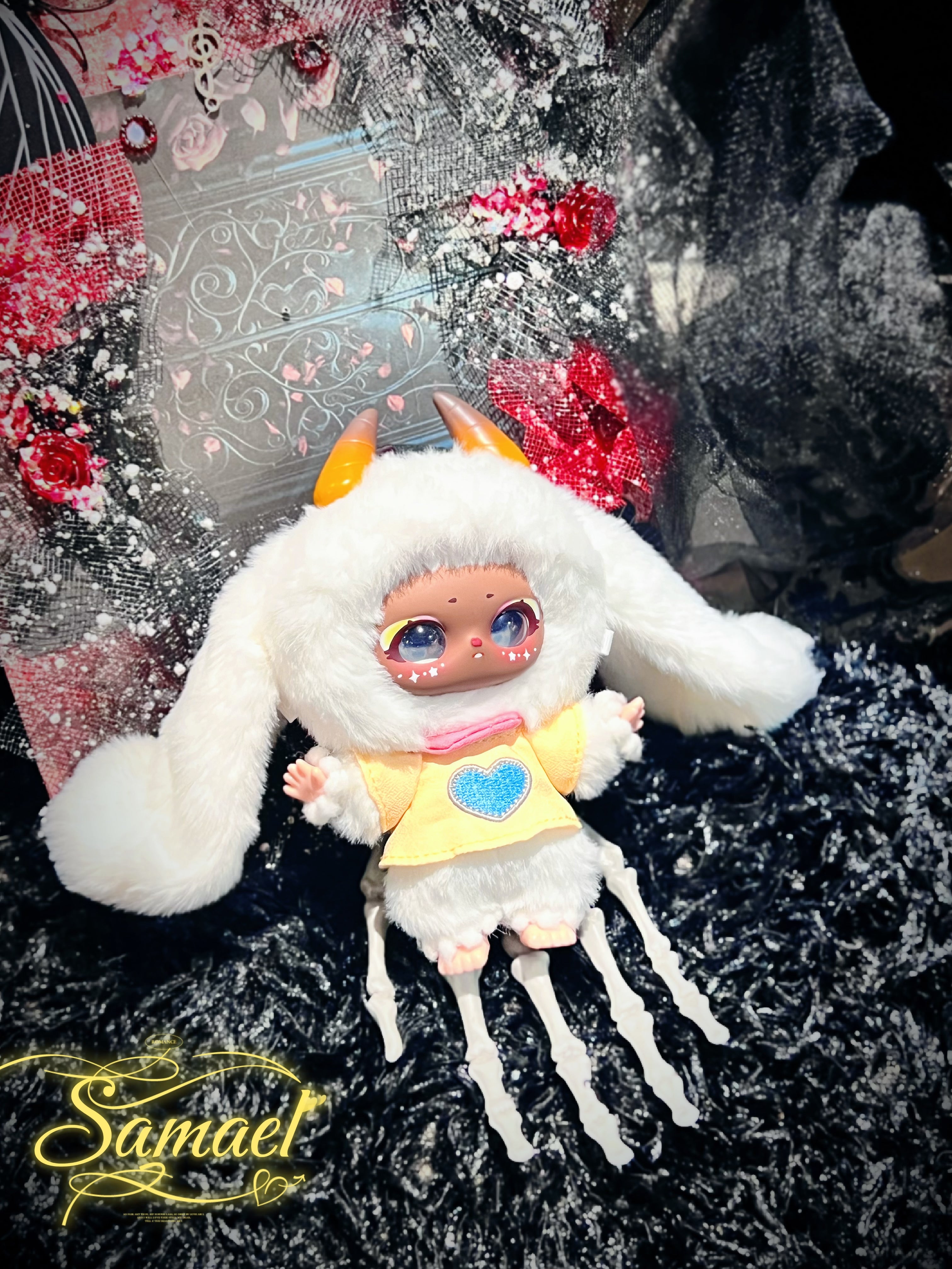 Baby Three - Shamali Magic Wardrobe art-doll in fluffy rabbit-eared hood, yellow shirt, posed on skeletal hand, surrounded by decorative elements, from Strangecat Toys.