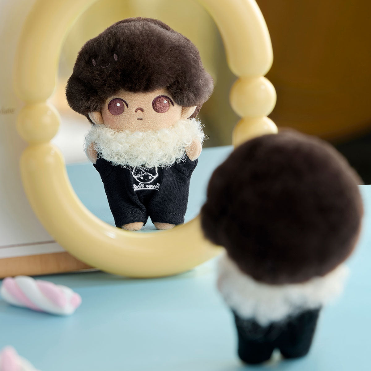 DIMOO Crush on Coffee Series plush keychain, featuring a fluffy afro and white scarf, reflected in a mirror with a pastel candy beside it.