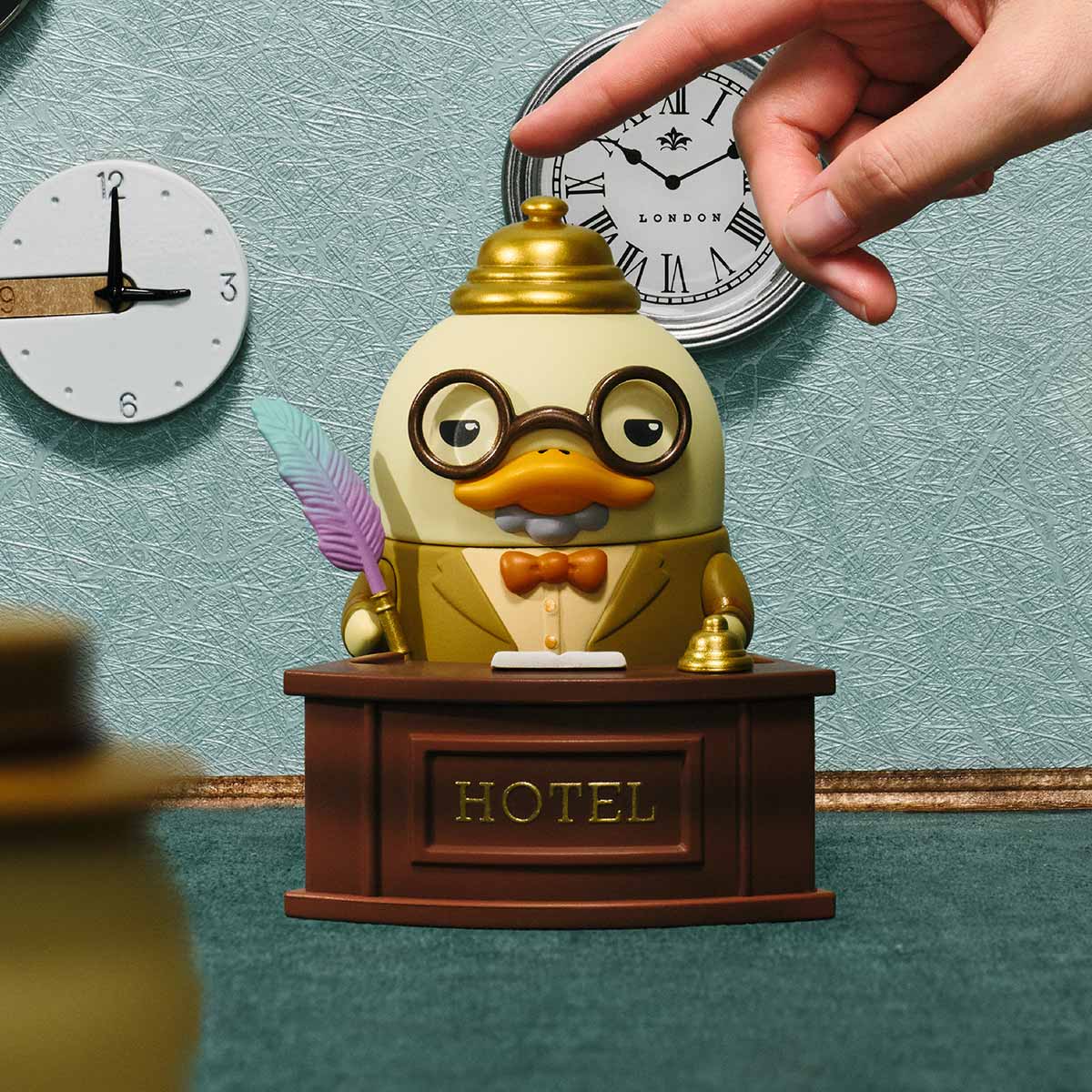 The Grand DUCKOO Hotel Series Figures - Preorder features a duck figurine as a hotel receptionist with spectacles, bow tie, and a service bell.