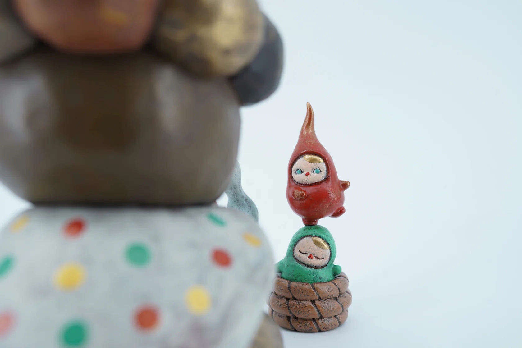 The Beanie Charmer - X-Mas Edition by Pucky figurines; a green sleepy gnome in a basket with a red, wide-eyed figure balanced atop.