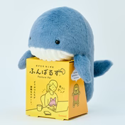 Posture Pal - Marine plush whale toy on a yellow box, featuring cartoon illustrations. A desk companion designed for posture support and comfort.