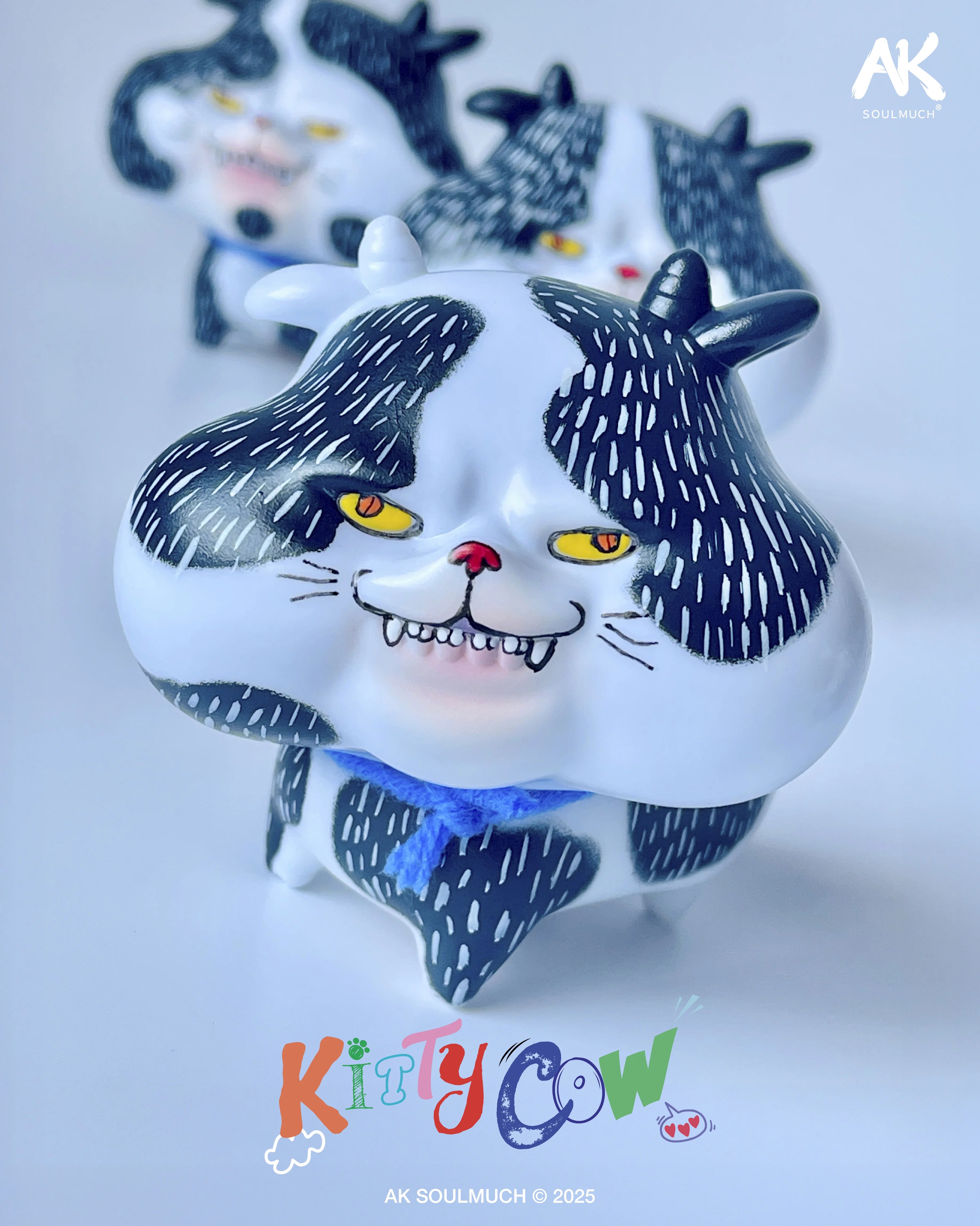 Kitty Cow art-toy figure by AK SOULMUCH, featuring a chubby creature with spotted fur, horns, yellow eyes, and a blue yarn collar, 140mm Sofubi.