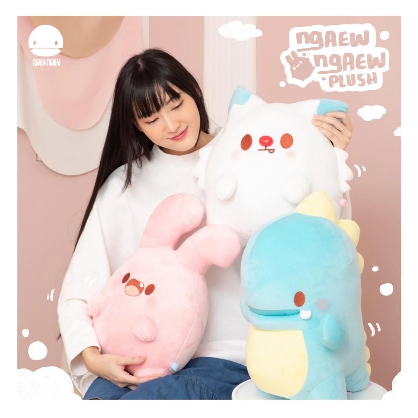Young woman holds three Ngaew Ngaew Plush toys: a pink bunny, white cat-like creature, and blue dinosaur, each 40-45 cm, against a pale pink backdrop.