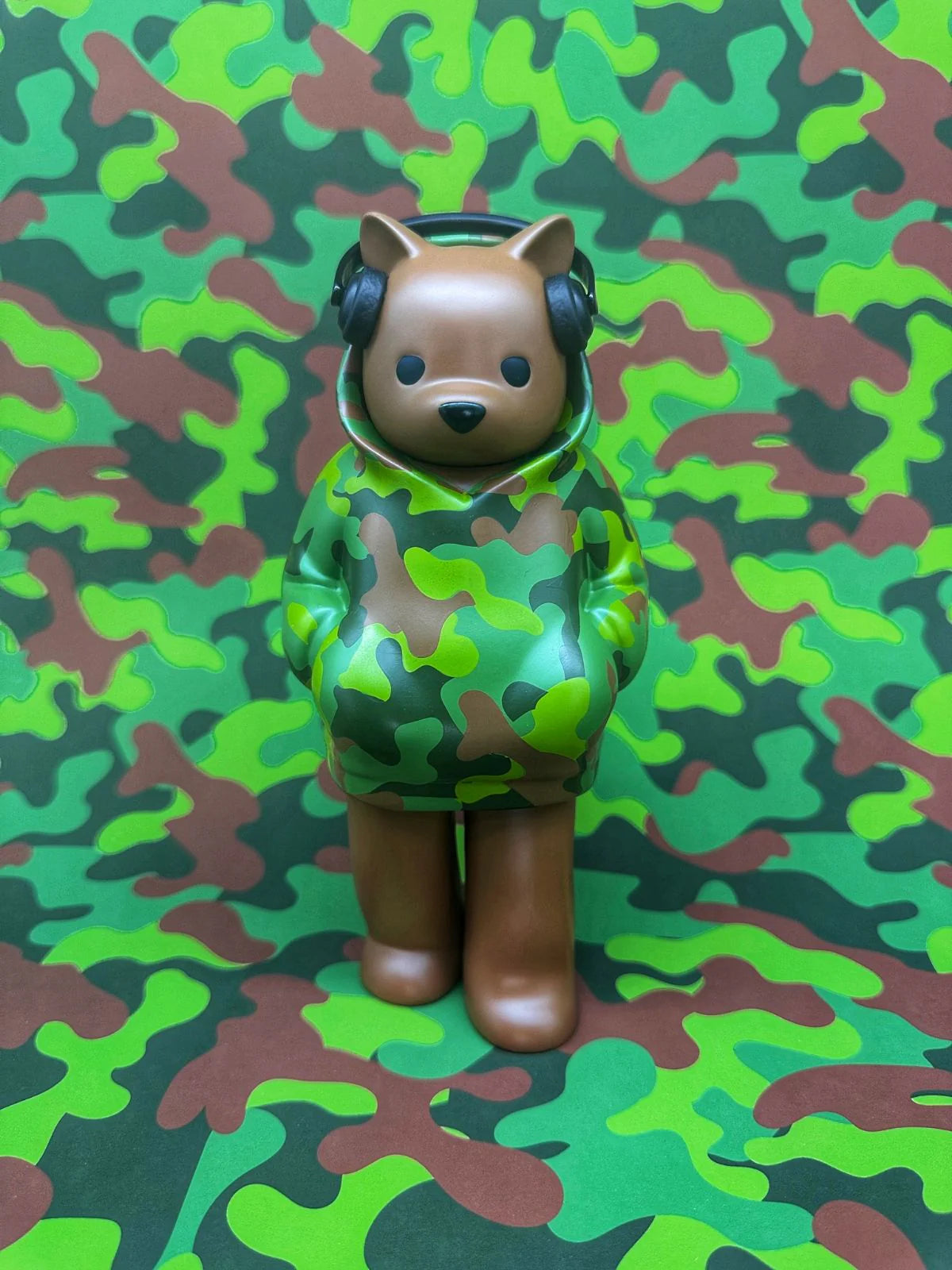 Low Fidelity - One With Nature by Luke Chueh: A 7-inch vinyl figurine of a camouflaged animal in a hoodie with headphones, blending into its patterned surroundings.