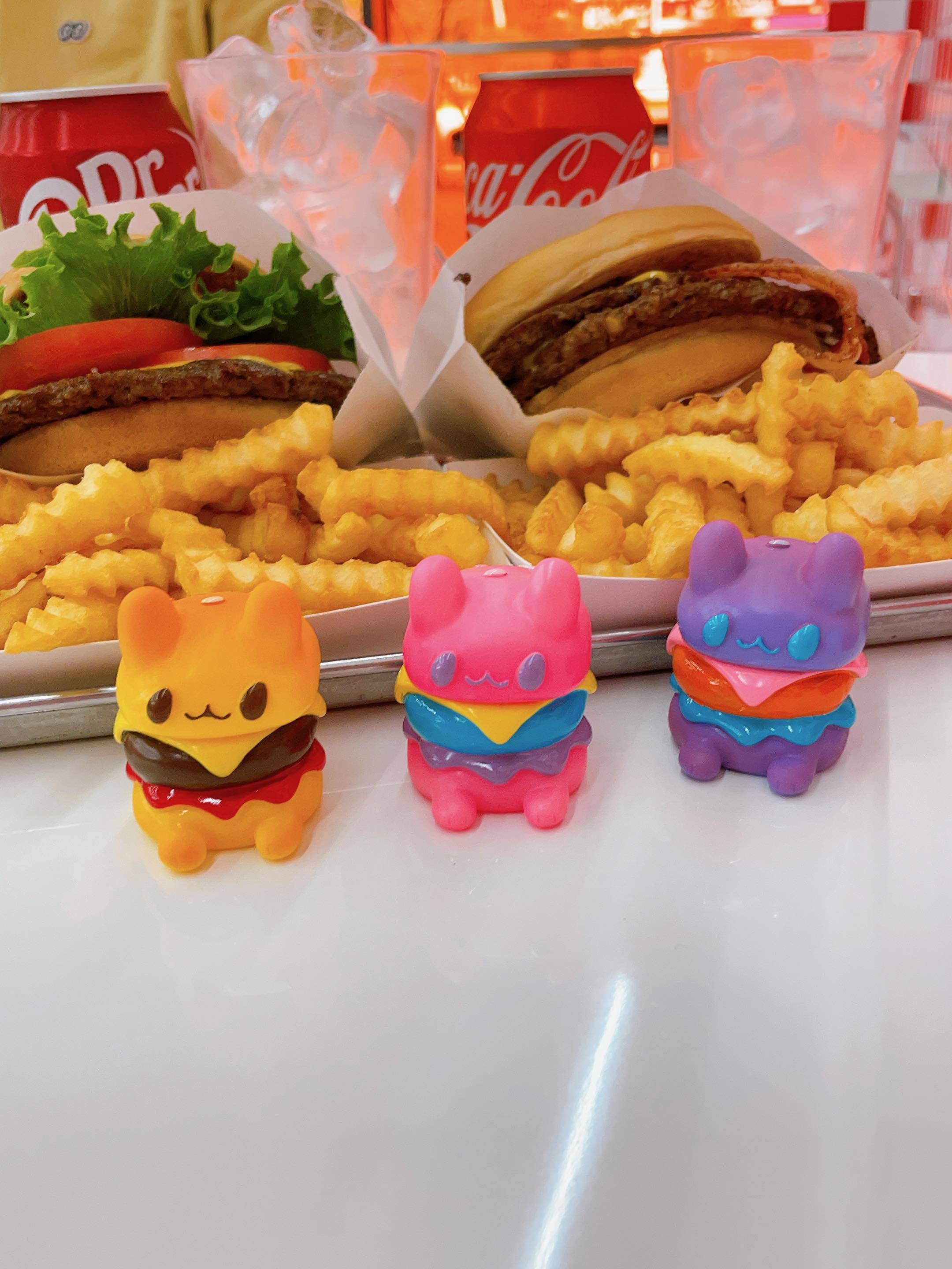 Baby Burgercat by Rato Kim surrounded by fast food toys and snacks on a plate.