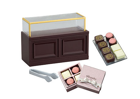 Chocolaterie Re-ment Blind Box Series: miniature chocolate-shop display with case, assorted chocolates, silver tongs, and a pink gift box for dollhouse collectors.