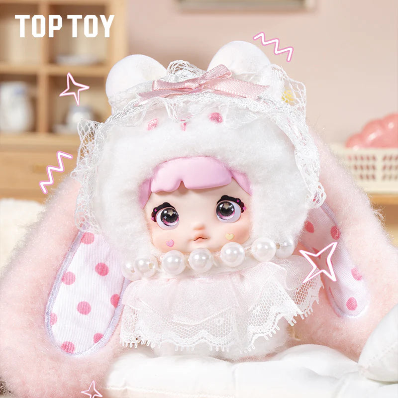 Nommi Baby Sweetheart Bunny Plush, a pastel toy doll with pink hair, big eyes, fluffy bunny hood, and heart decals, available for preorder.