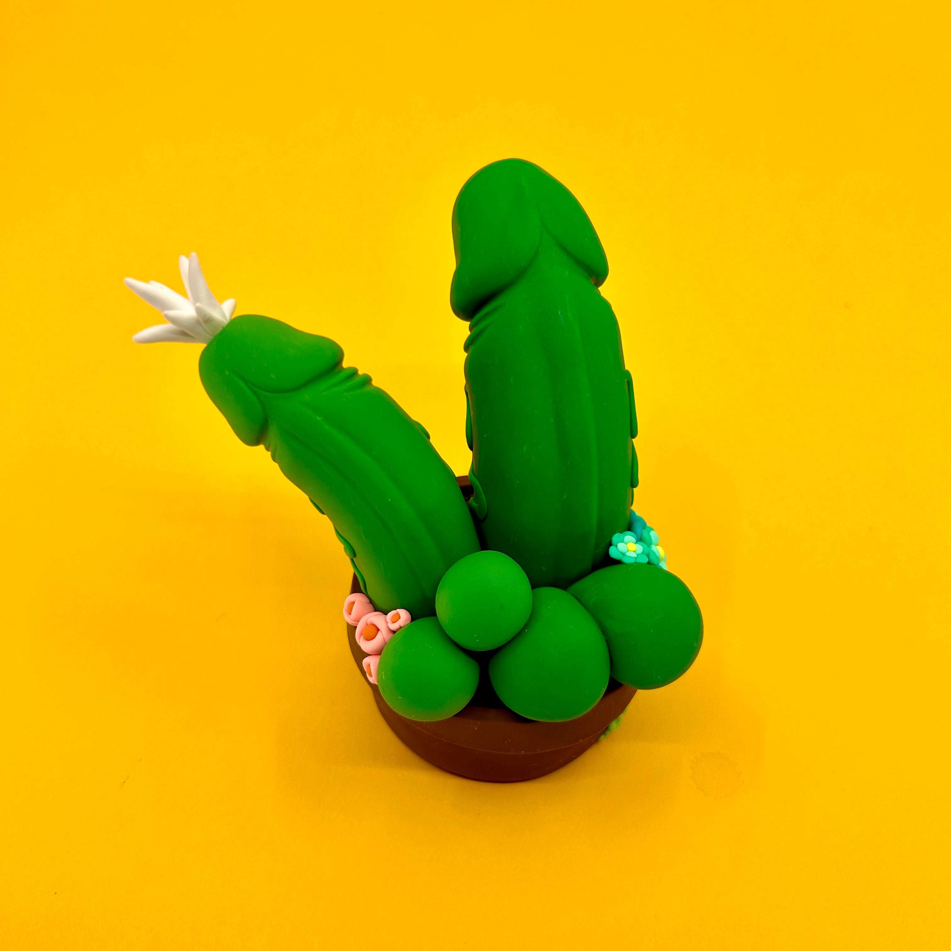 Polymer clay cactus in pot with flower and toy cucumber.