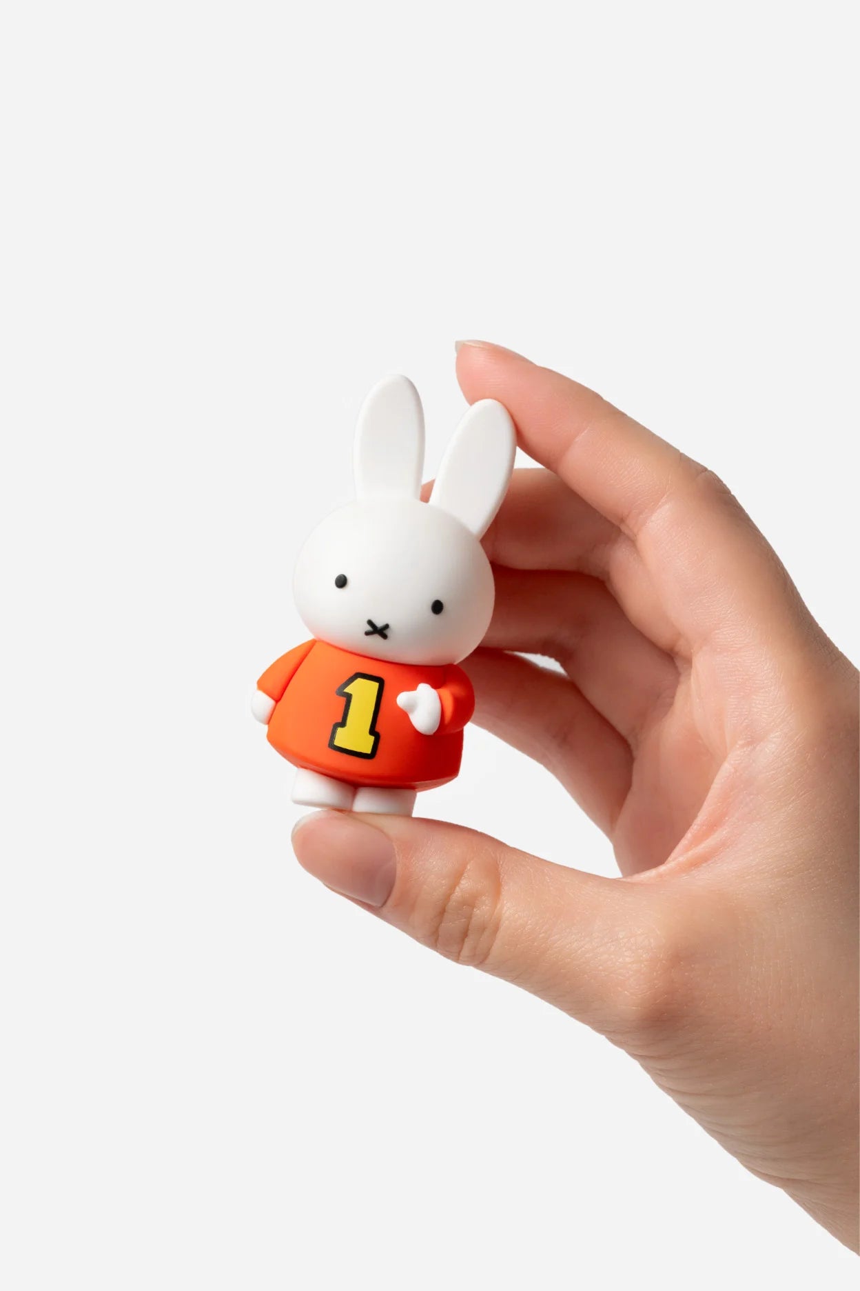 Smoko Miffy Dressing Up Blind Box Figure, a small vinyl rabbit in an orange sweater with a 1, held between fingers against a white background.