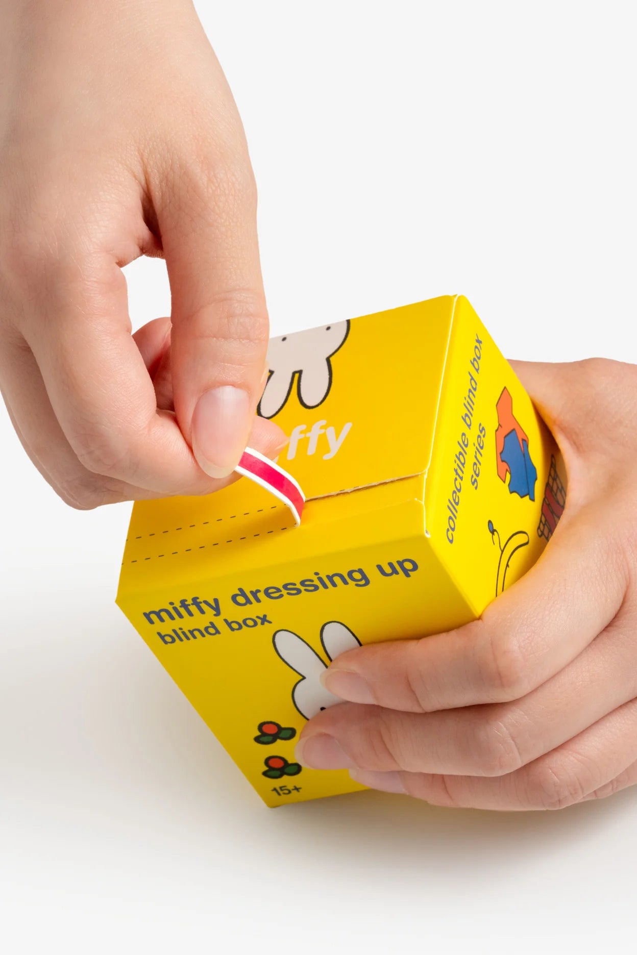 Hands opening a Smoko Miffy Dressing Up Blind Box Figure, featuring the Miffy character and text on a bright yellow package, part of a collectible series.