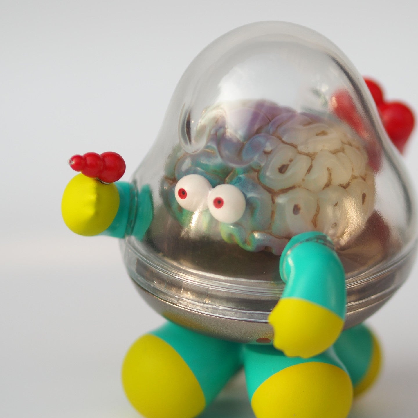 A toy with a brain and arms, Mr.Brain - Brains Attacks, in sofubi/resin, 9 cm tall. Close-ups of eyes, brain, and colorful elements. Preorder - Ships Late May 2024.