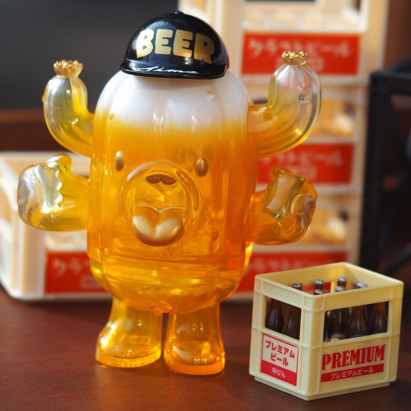A blind box toy titled BEER PATU, a 10 cm tall soft vinyl bear with a black hat, holding a crate of beer bottles. Preorder - Ships Late May 2024.