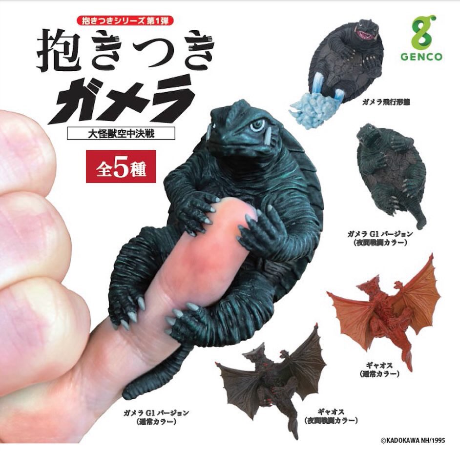 Toy lizard from Hugging Gamera: Guardian of the Universe Gacha Series, holding a hot dog, balanced on a thumb.