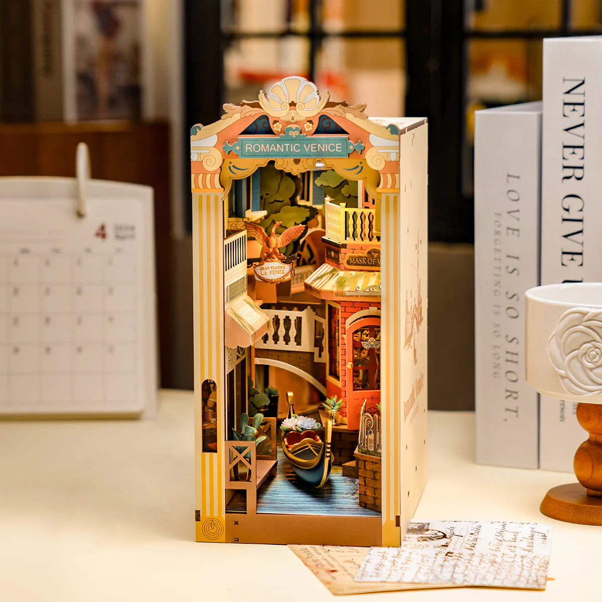 Rolife Romantic Venice DIY Book Nook Shelf Insert Kit TGB08 featuring a miniature Venice scene with a canal and landmarks beside a calendar on a table.